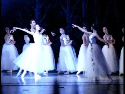 Kaitana Magno performing in Giselle. Ballet dancers performing on stage with one dancer in front, wearing a white tutu, and others in the background dressed similarly, set against a dark backdrop.