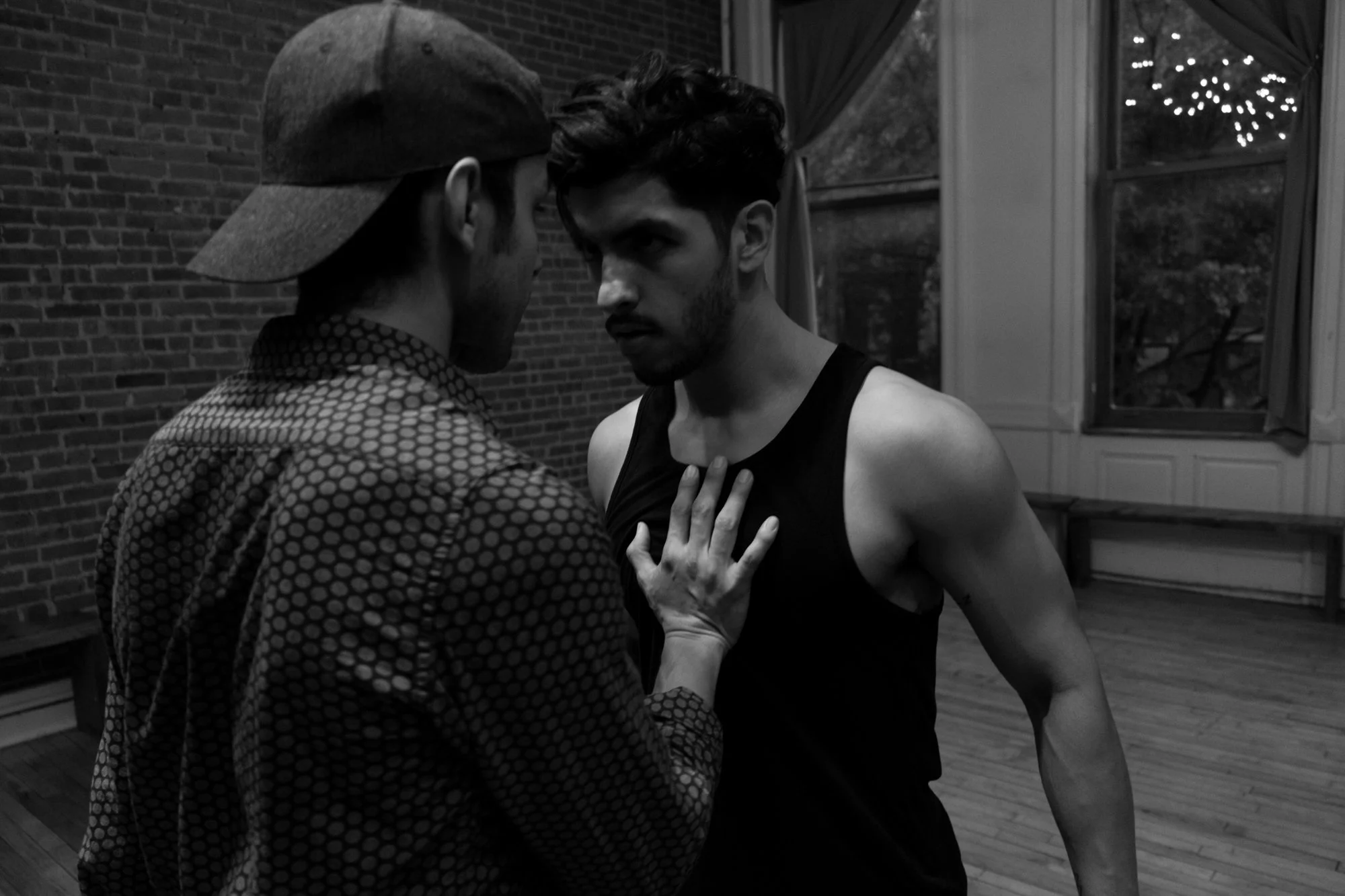 Immersive dance scene. Kaitana Magno and Jimmy Sutherland coach two men in an intense confrontation indoors. One man is close and whispering, while the other, in a sleeveless shirt, has a tense expression and is touching his chest.