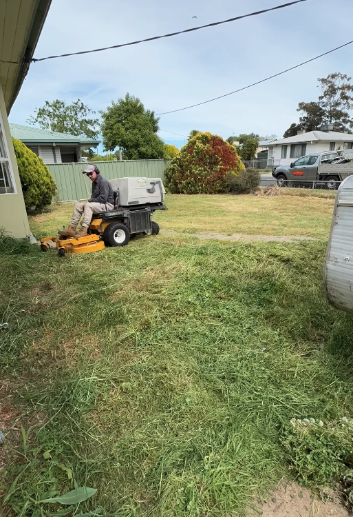 Person operating a ride-on lawn mower in a backyard, cutting the grass near the house