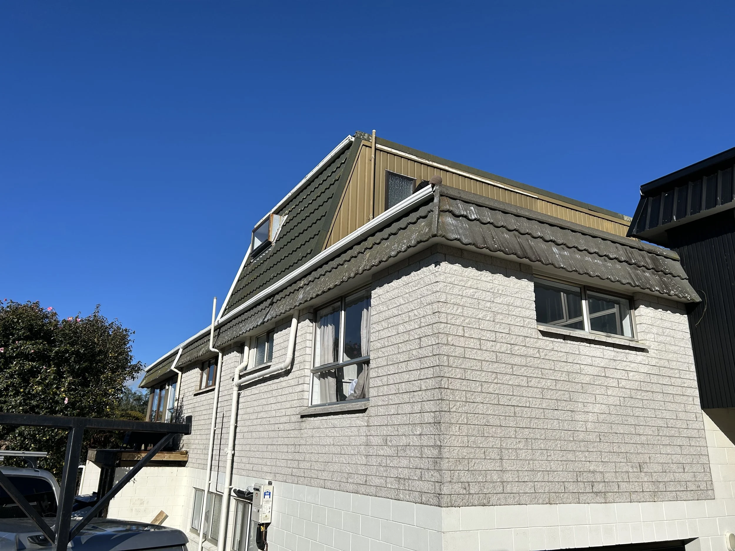 A two-story residential building with white brick lower walls and a textured gray upper wall, featuring multiple windows, set against a clear blue sky.