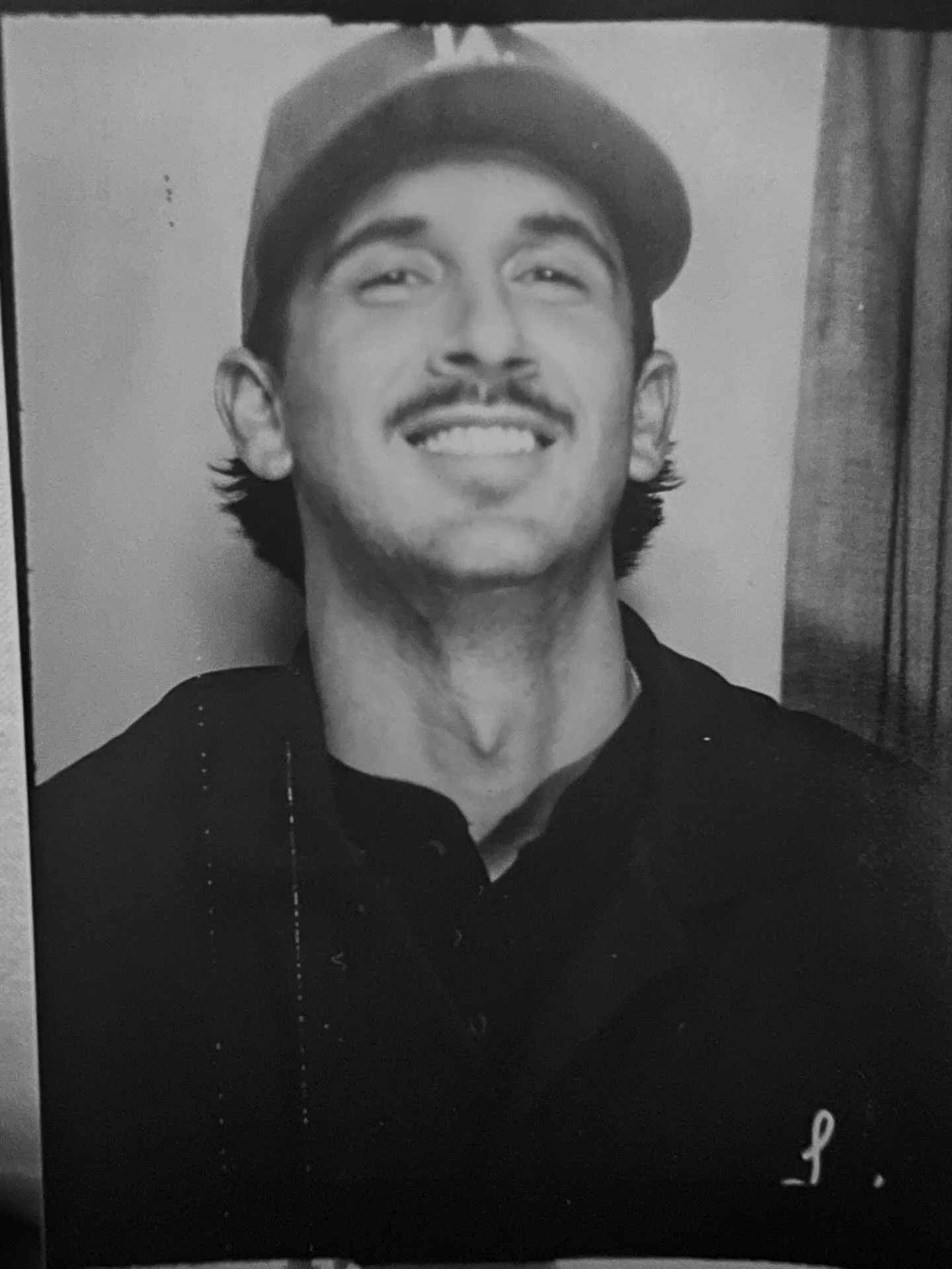 A man dressed as a golfer, wearing a white golf shirt and a dark green cap with sunglasses, standing outdoors on a sunny day with trees in the background.