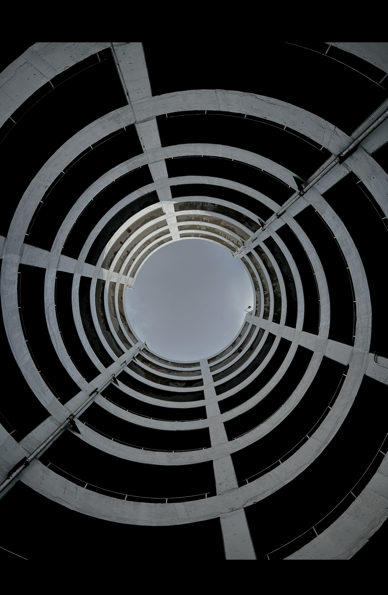 Looking up inside a multi-story parking garage with circular open levels and a cloudy sky at the top.