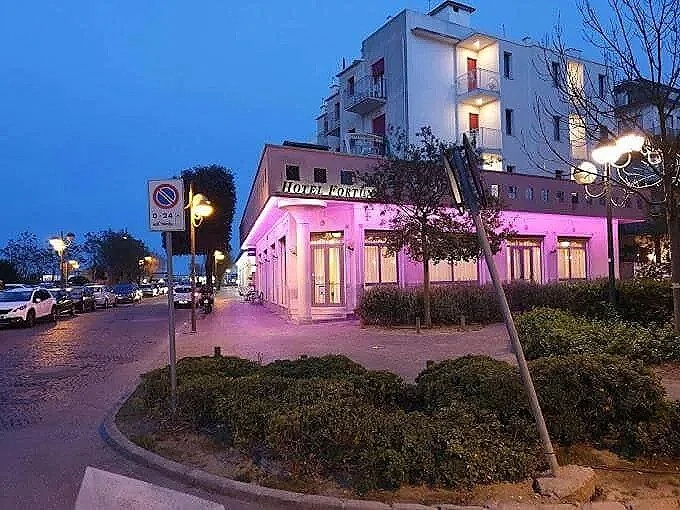 Edificio con luci rosa, segnale di divieto di sosta, strada, lampioni e auto parcheggiate di sera.