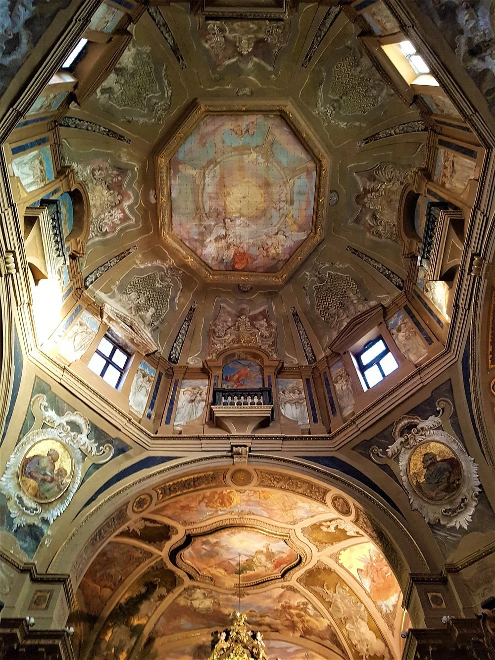 Interno di una chiesa con affreschi ornati e un soffitto a volta decorato con scene religiose e un grande lampadario dorato.