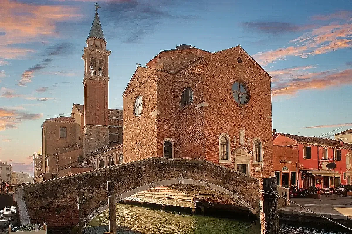 Un antico edificio in stile veneziano davanti a un canale con un ponte in pietra, al tramonto.