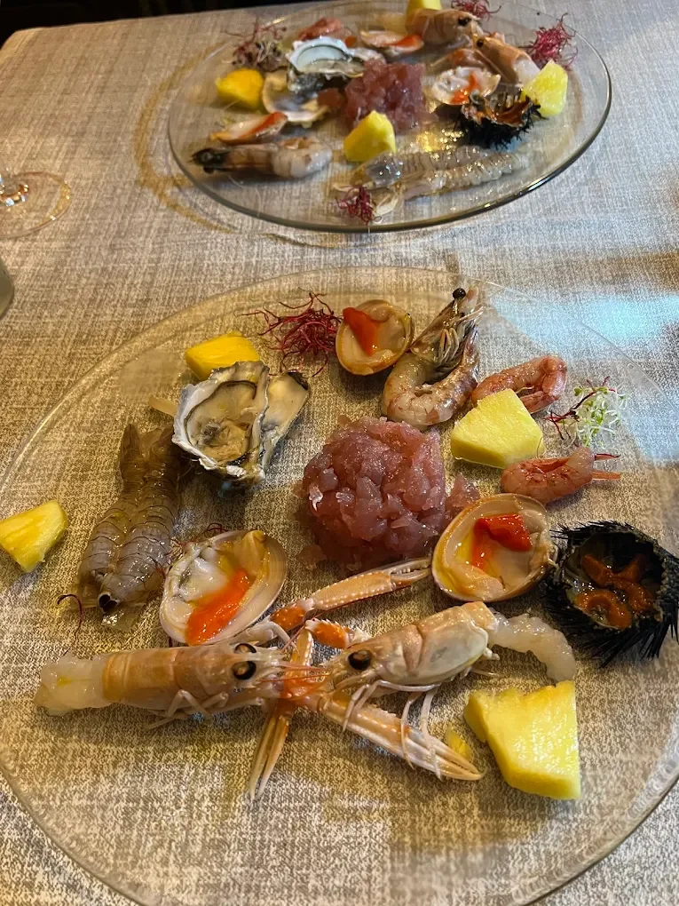 Piatti di crudo di mare con gamberi, ostriche, polpa di tonno, e frutta come ananas, serviti su piatti di vetro.