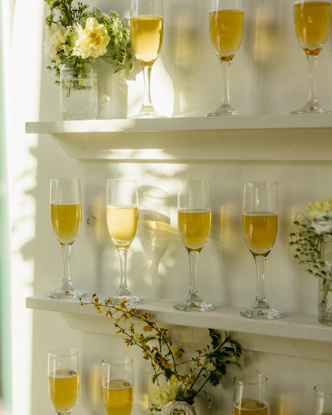 Multiple glasses of champagne on white shelves decorated with flowers