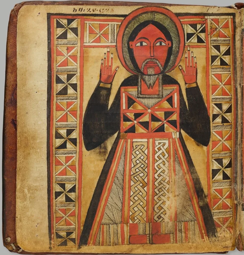 A traditional religious icon depicting Jesus Christ with a halo, raising both hands in a blessing gesture, wearing a patterned robe, with a geometric border in red, black, and gold.