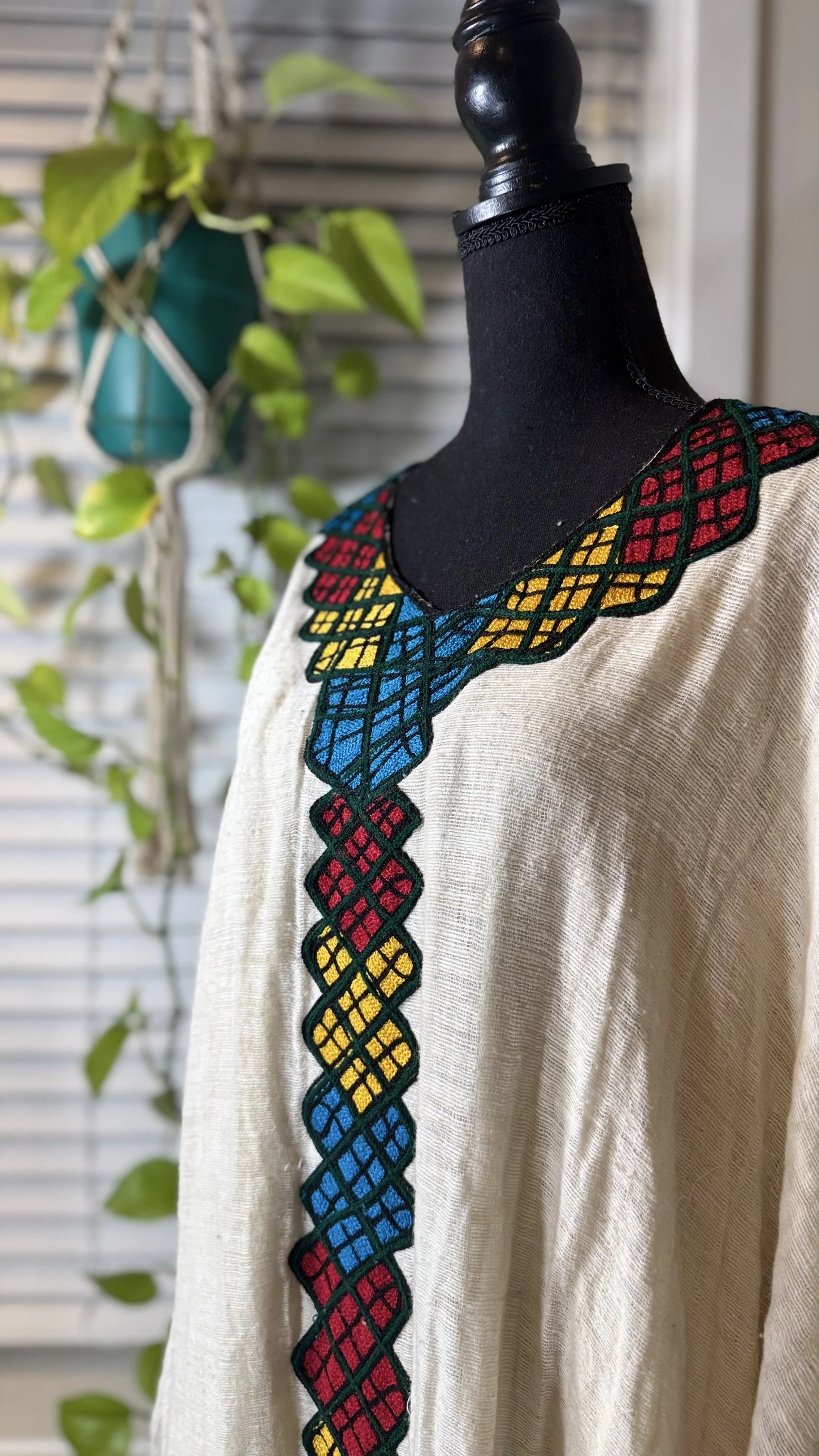 Beige embroidered blouse with colorful geometric embroidery on the neckline and down the front displayed on a black mannequin.