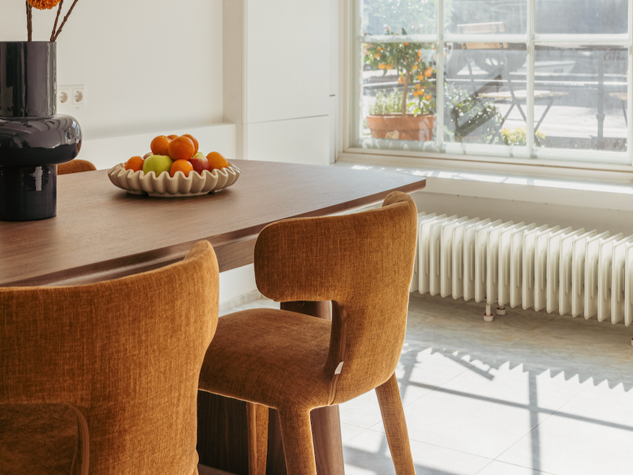 Een eetkamertafel met een groentebord en een vaas met bloemen, naast een grote raam met uitzicht op een tuin.