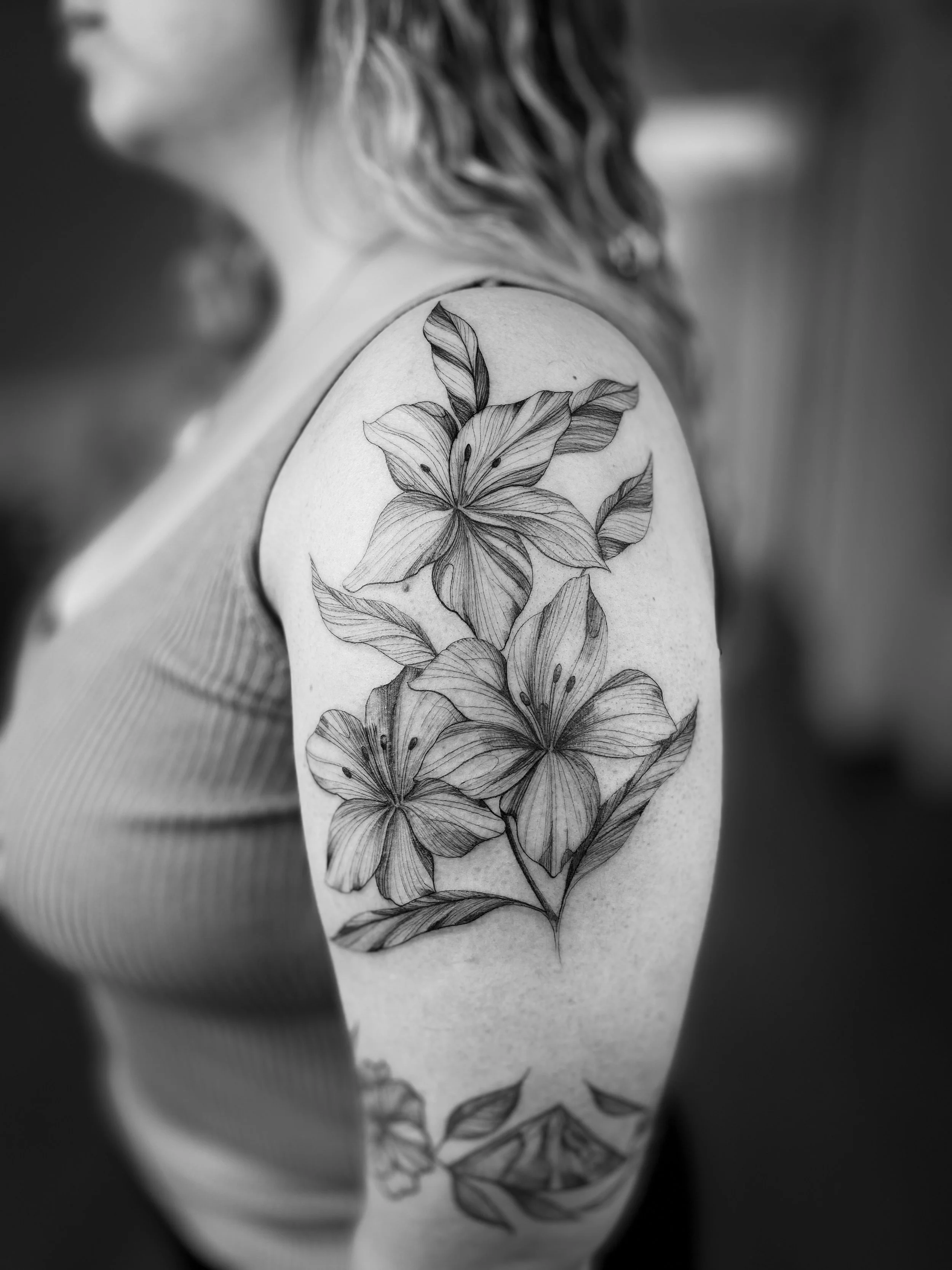 Tatuaje en el hombro de una mujer, con diseño de flores y hojas en tonos oscuros.