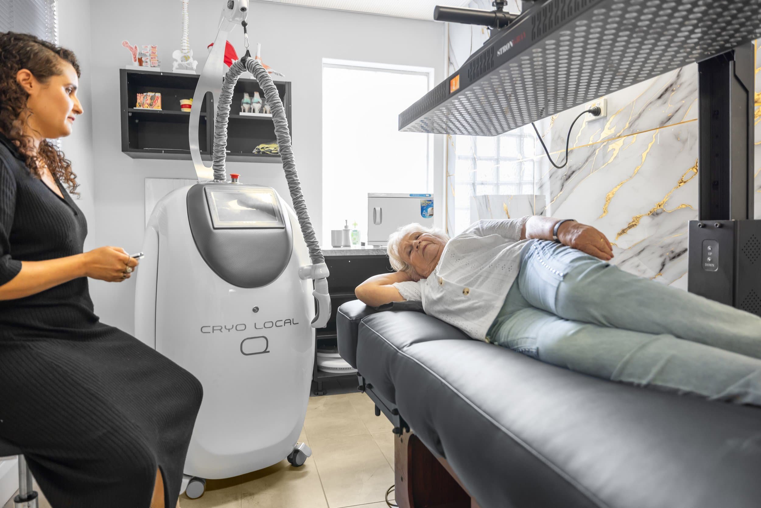 An elderly woman lying on a medical examination table, receiving cryotherapy treatment from a healthcare professional at Strongray health and wellness centre