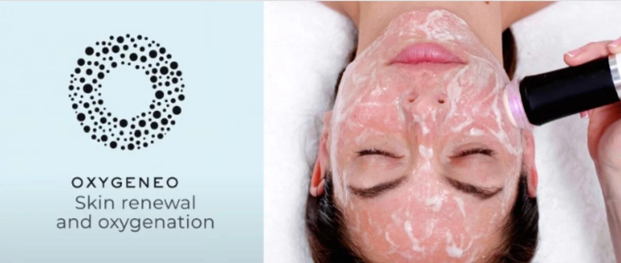 A woman receiving a facial treatment with a device in a spa or clinic setting, with a close-up view of her face covered in a cream or mask, and the left side displaying a logo and text that reads "OXYGENEO Skin renewal and oxygenation."