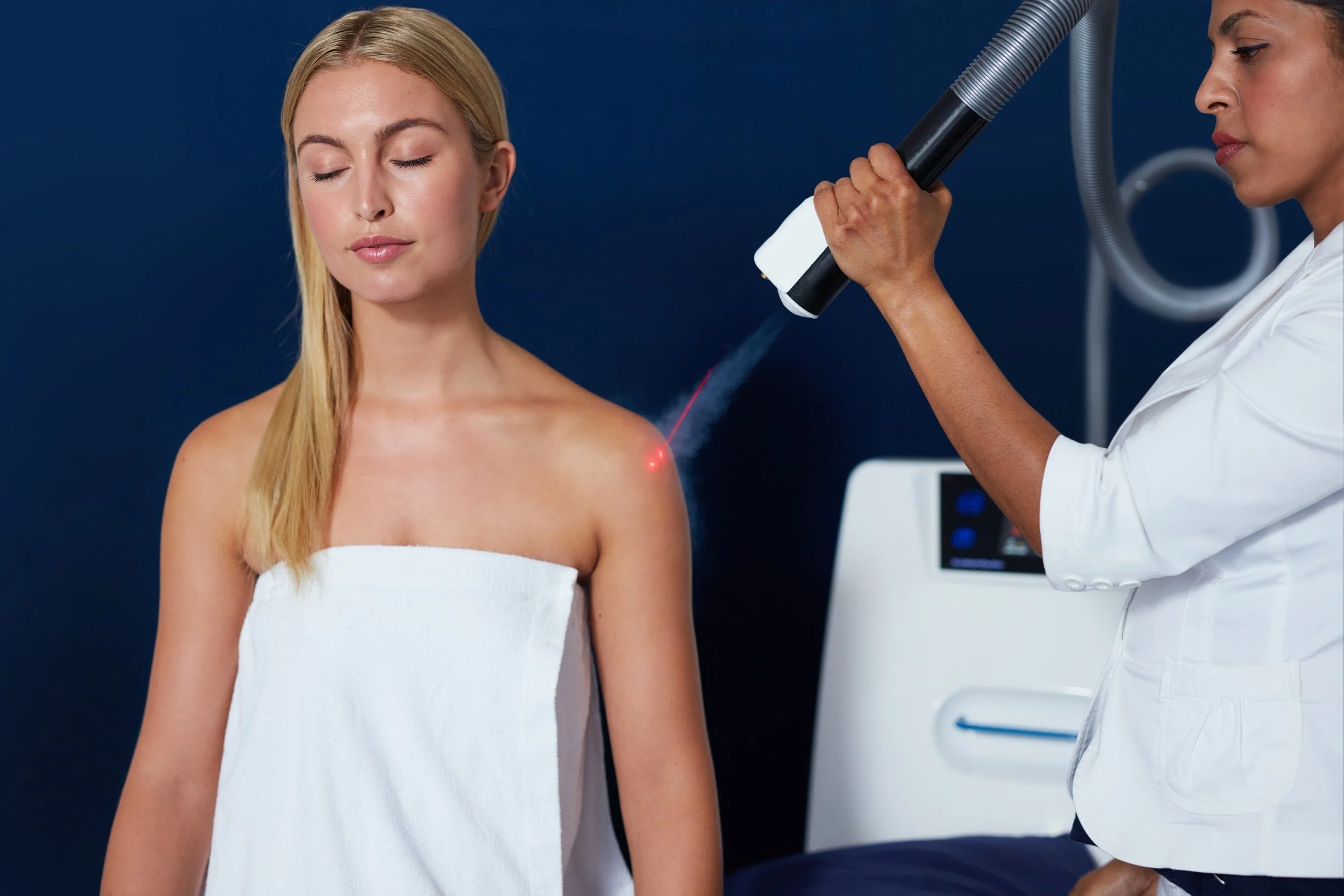 A woman receiving cryotherapy treatment on her shoulder from a healthcare professional in a health & wellness setting.