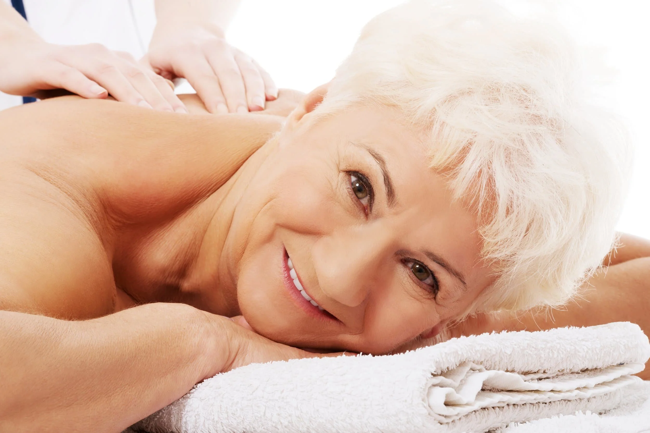 A smiling woman with short, white hair receiving a back massage.