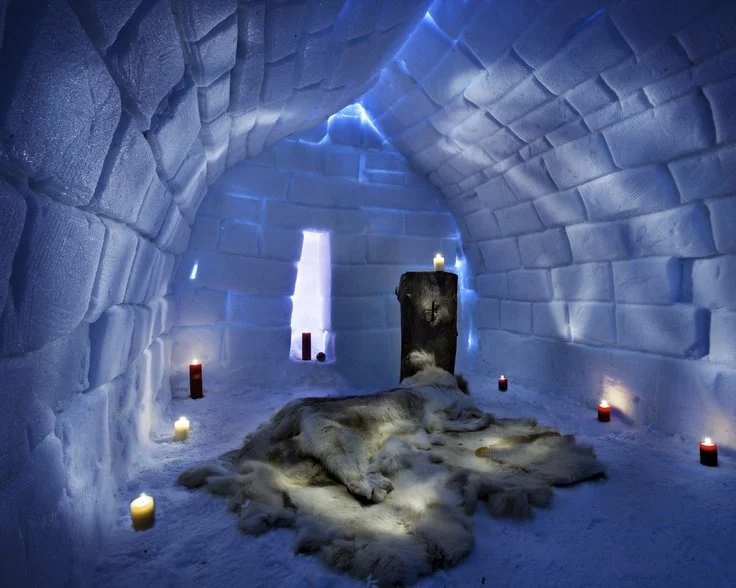 Inside an igloo with a fur rug in the center, lit by candles and a small window shaped like a cross.