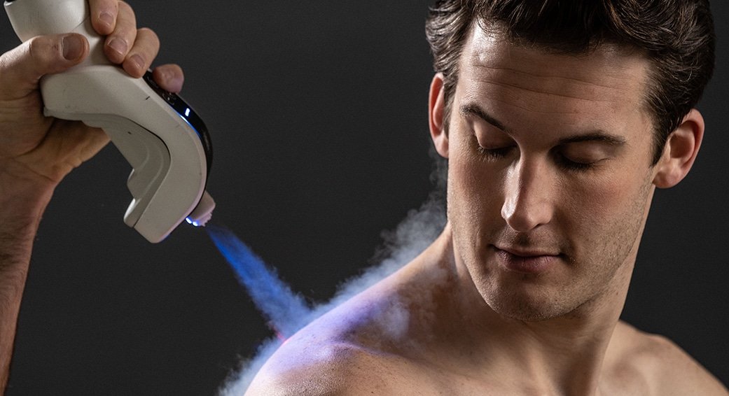 A man receiving a laser treatment on his shoulder from a handheld device, with visible laser light and vapor or steam.