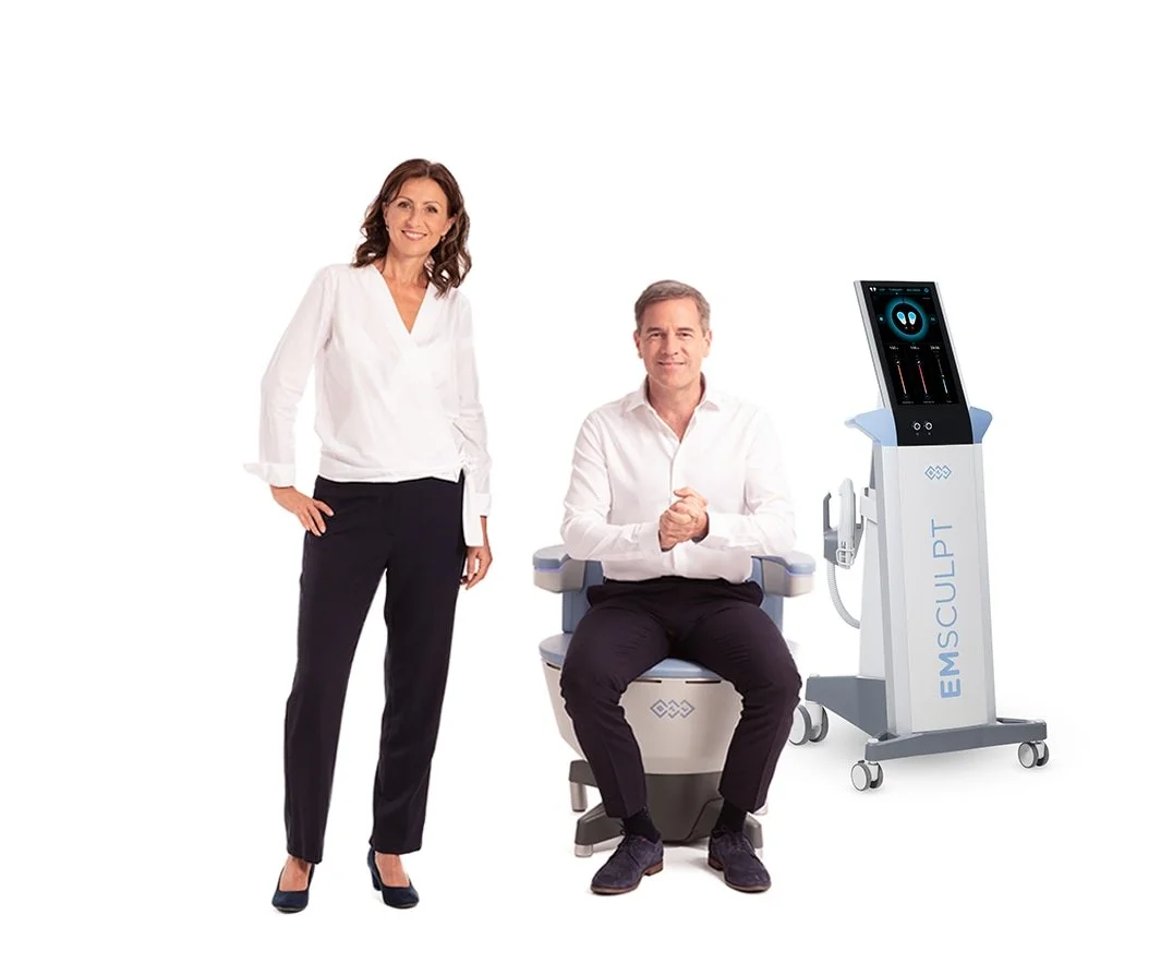 A woman standing in white blouse and black pants next to a seated man in white shirt and black pants, with an EMSELLA medical device beside them.
