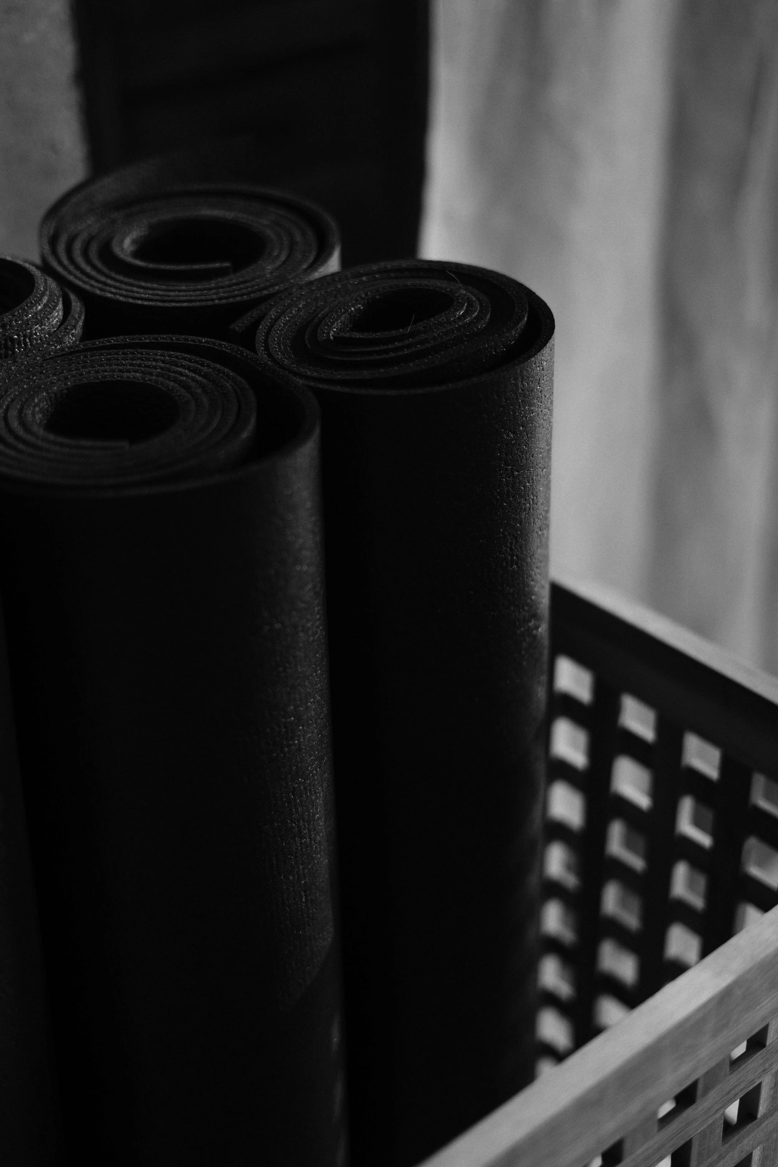 Four rolled-up black pilates mats in a basket.