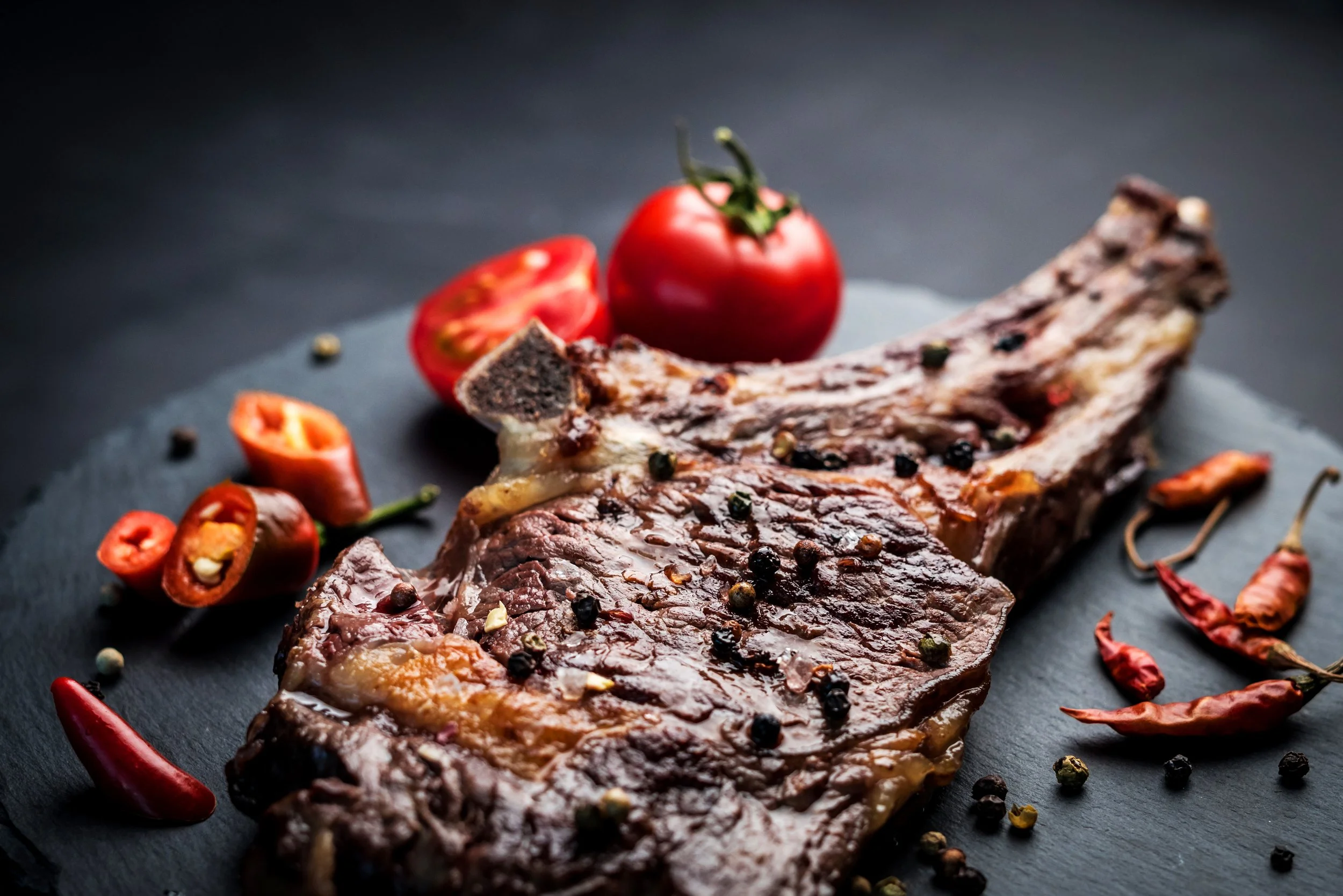Corte de carne asada con pimienta, especias y tomates cherry en un plato oscuro.