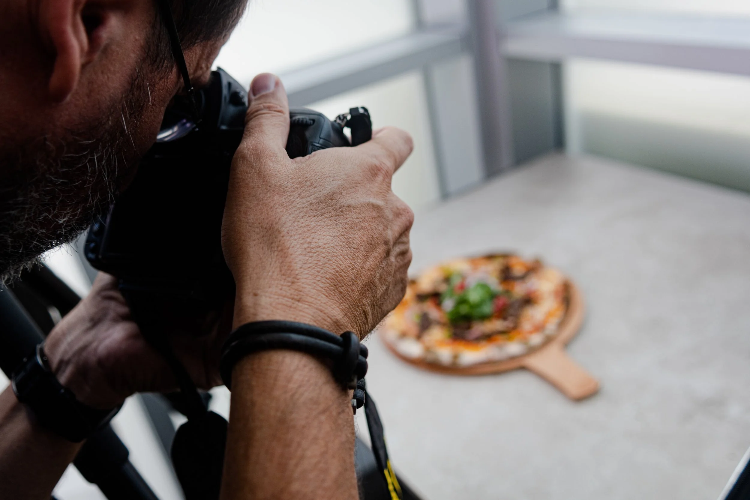 Un hombre tomando una foto de una pizza en una mesa de concreto.
