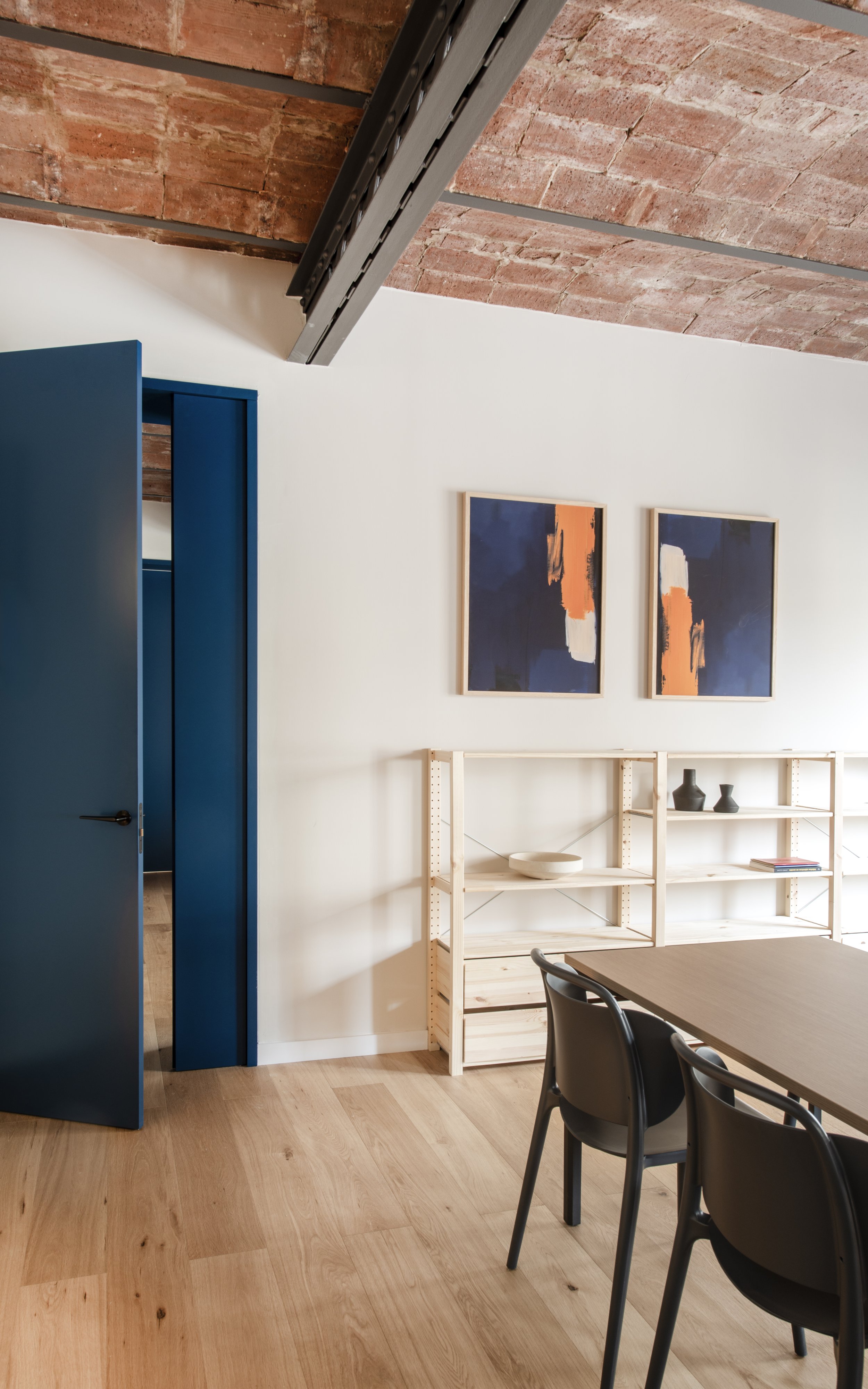 Detalle de puerta azul petróleo, estantería de madera y obra de arte en Vértigo Vida, Barcelona. Interiorismo estratégico para espacios terapéuticos por Escabeche Studio.