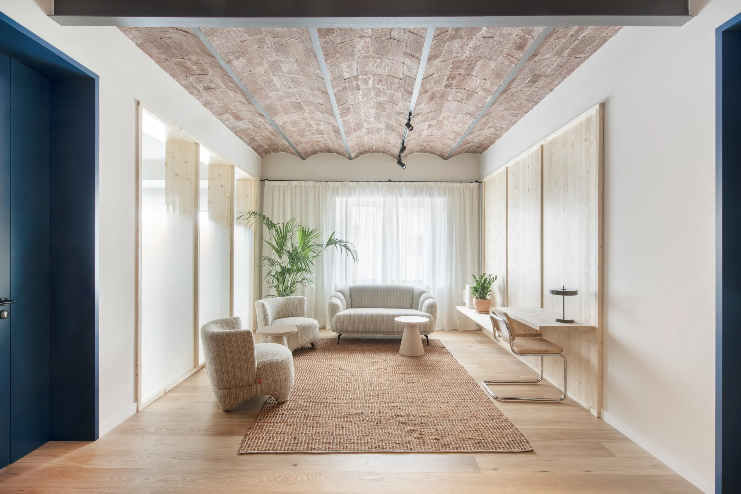 Sala de estar luminosa de Vértigo Vida con sillones blancos, alfombra natural y vegetación. Centro terapéutico de día en Barcelona, proyecto de Escabeche Studio.