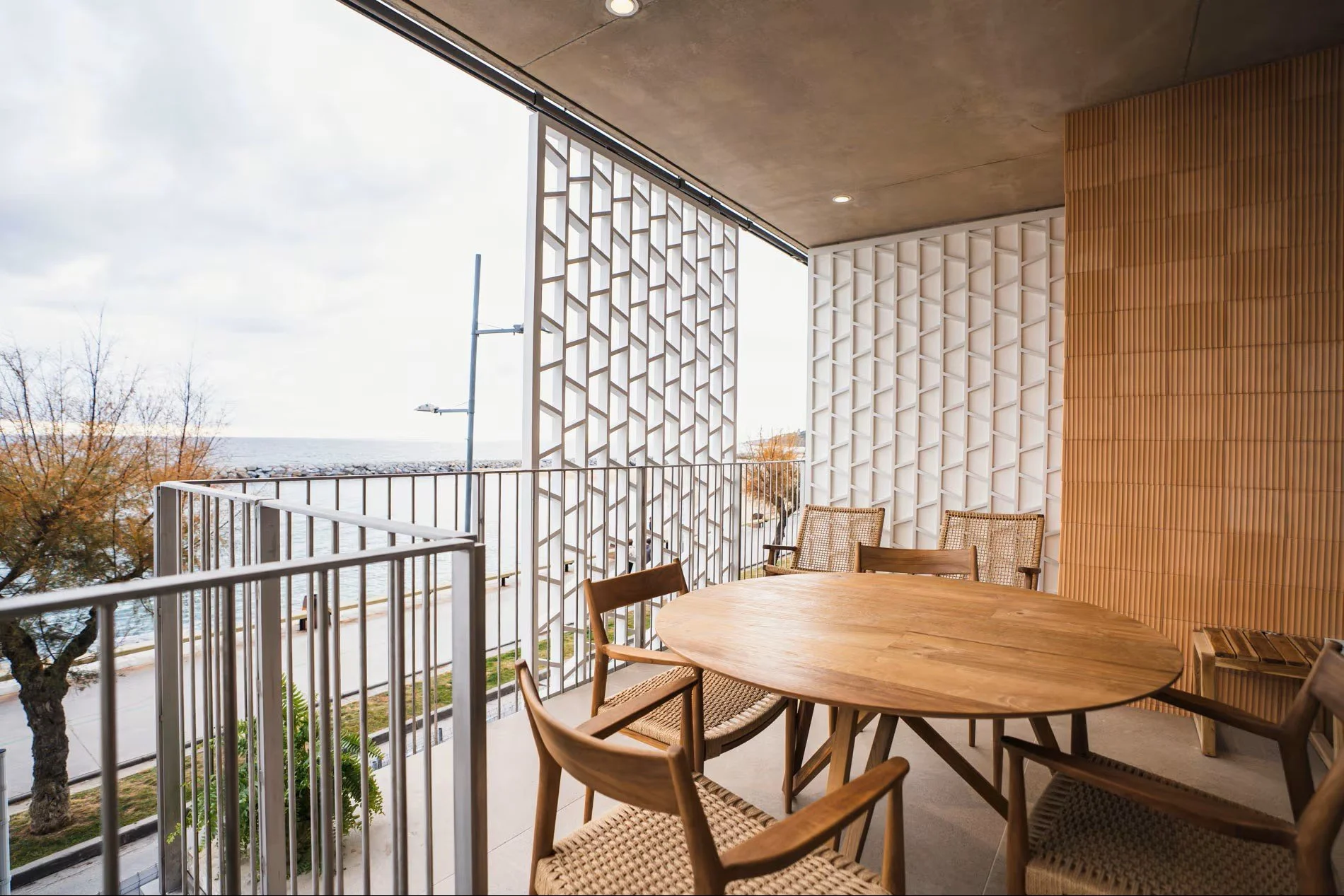 Terraza con mesa y sillas de madera y celosía calada en Sorra Mar i Cel, Costa Brava. Espacio exterior privado en apartamento turístico frente al mar. Proyecto de Escabeche Studio.