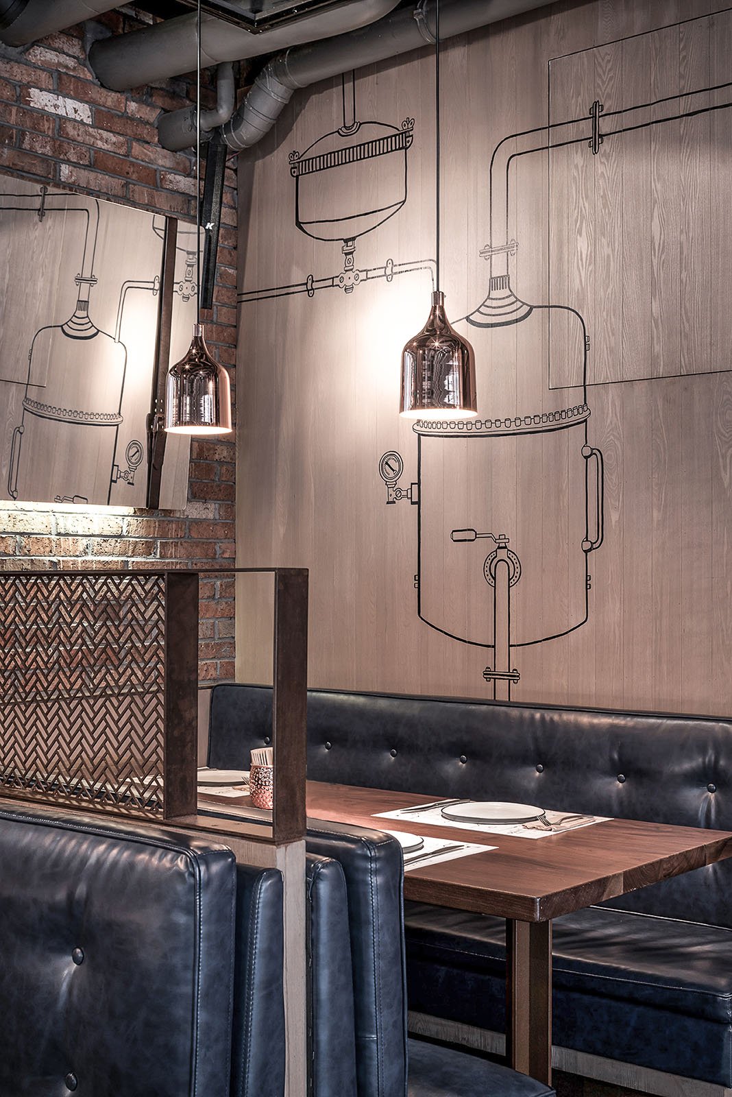 Respaldo de sillón y mesa en un restaurante con pared decorada con dibujo de equipo de destilación y lámparas de cobre suspendidas.