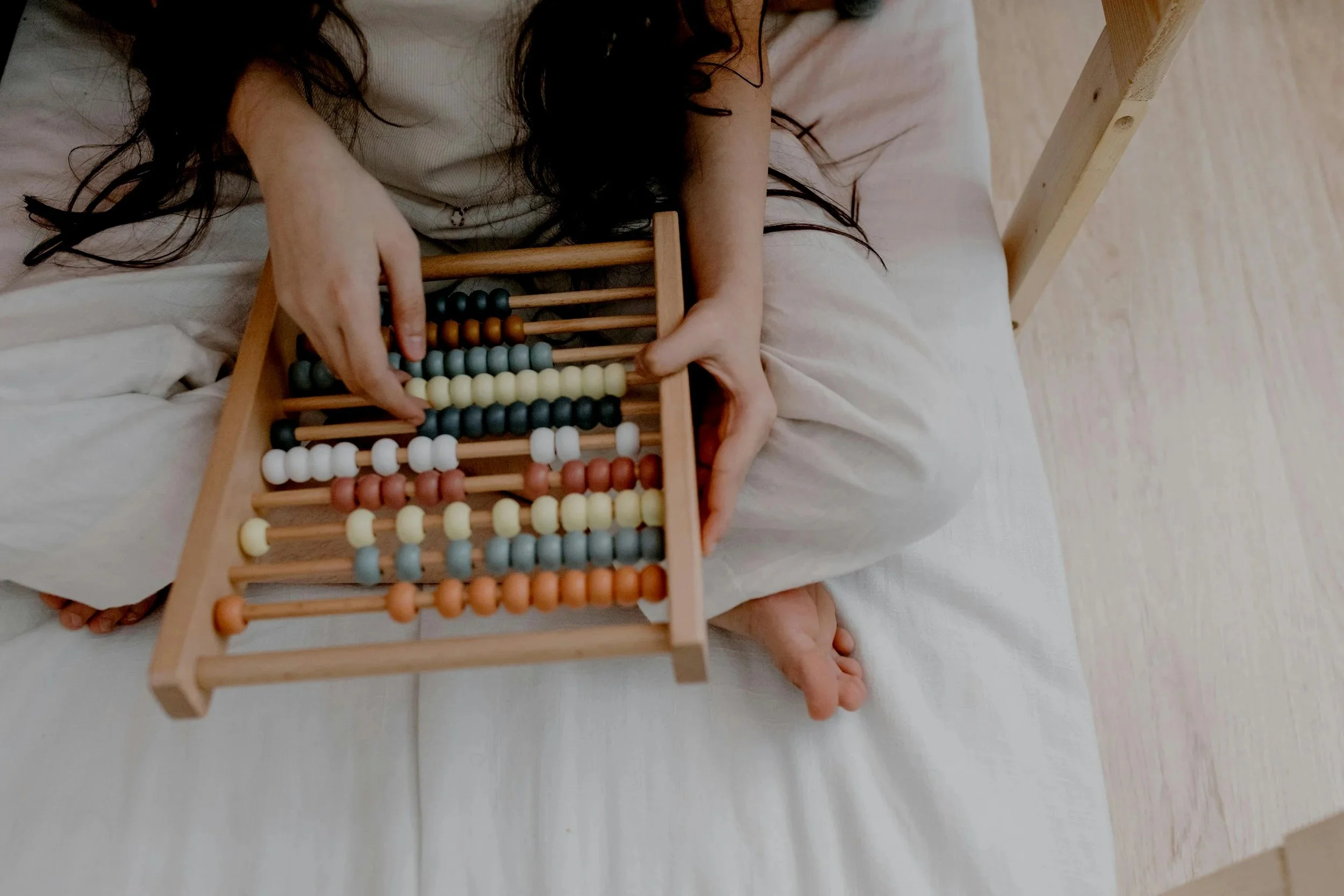Person with long dark hair sitting on a bed, using an abacus with colorful beads.