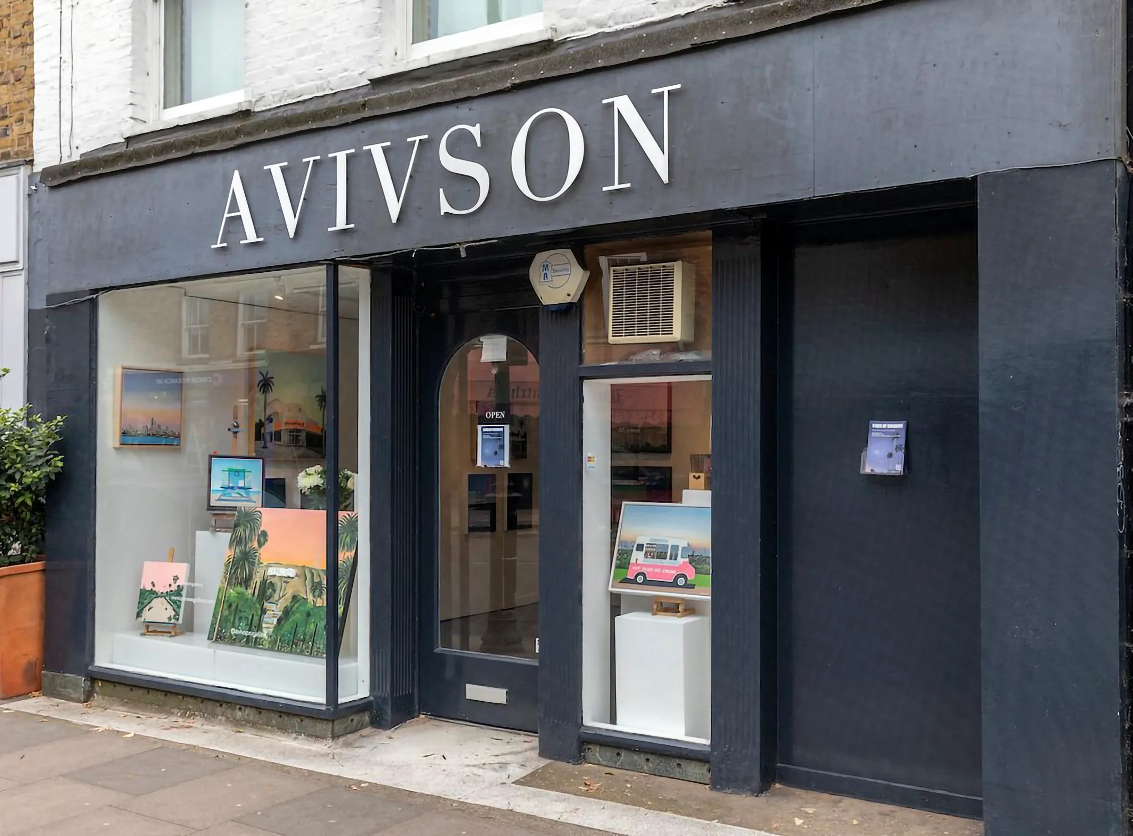 Art gallery named 'AVISSON' with paintings displayed in the large front window and on small easels outside, including landscape scenes and colorful artistic pieces.