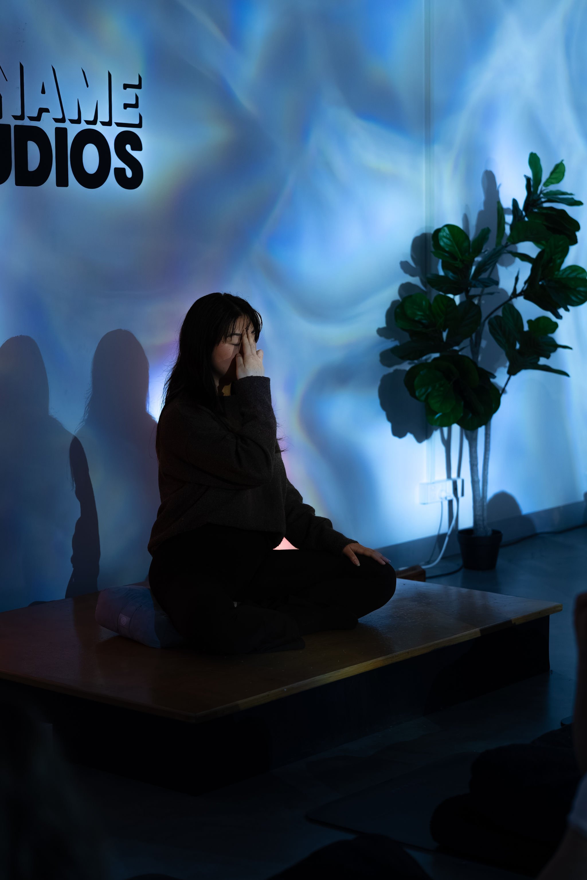 Liz Ho demonstrating alternate nostril breathing on stage at No Name Studios during a breathwork class.