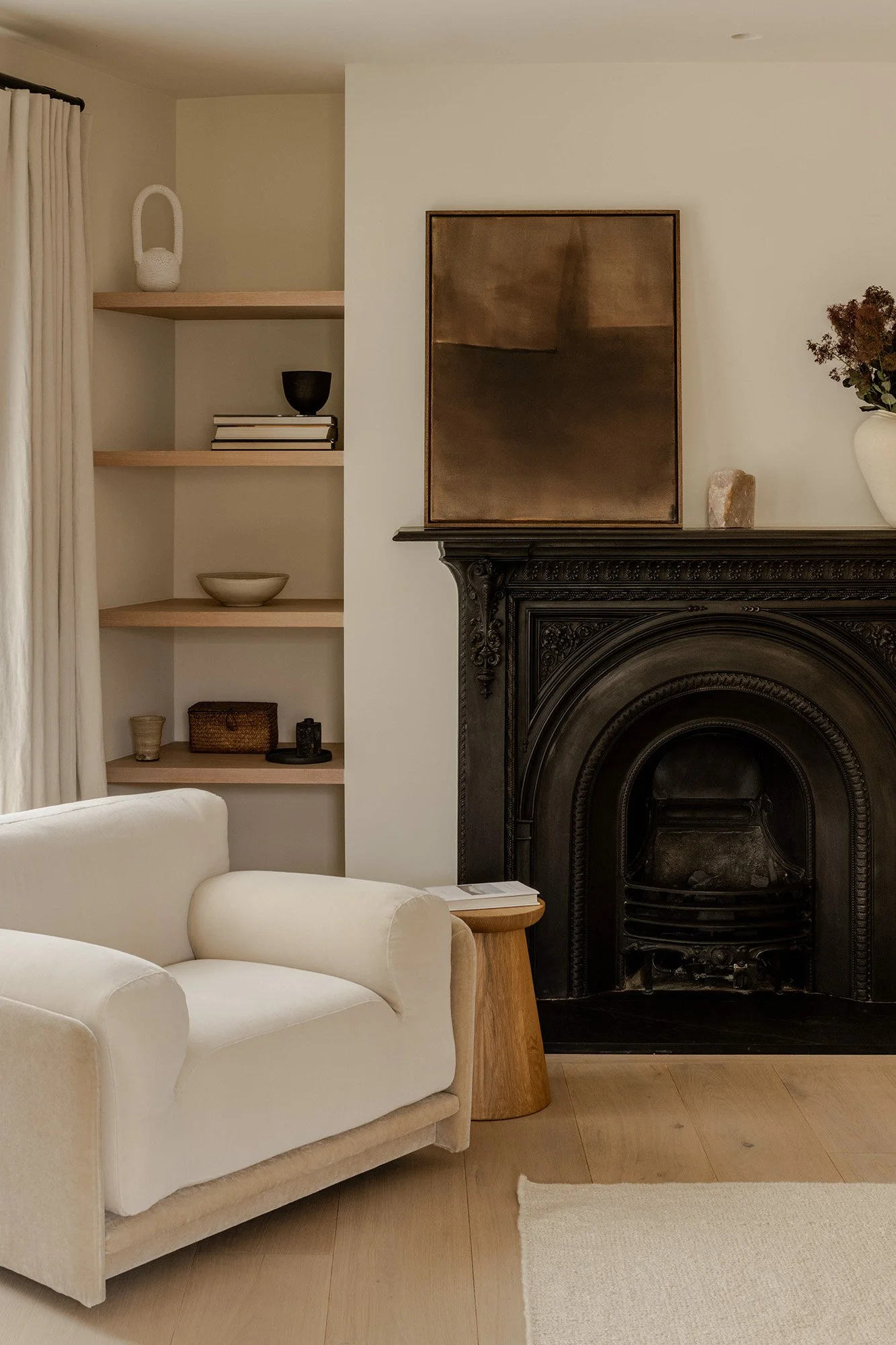 Living room with white sofa, wooden side table, a dark fireplace with decorative carvings, built-in shelves with decorative objects, and a large abstract painting above the fireplace.