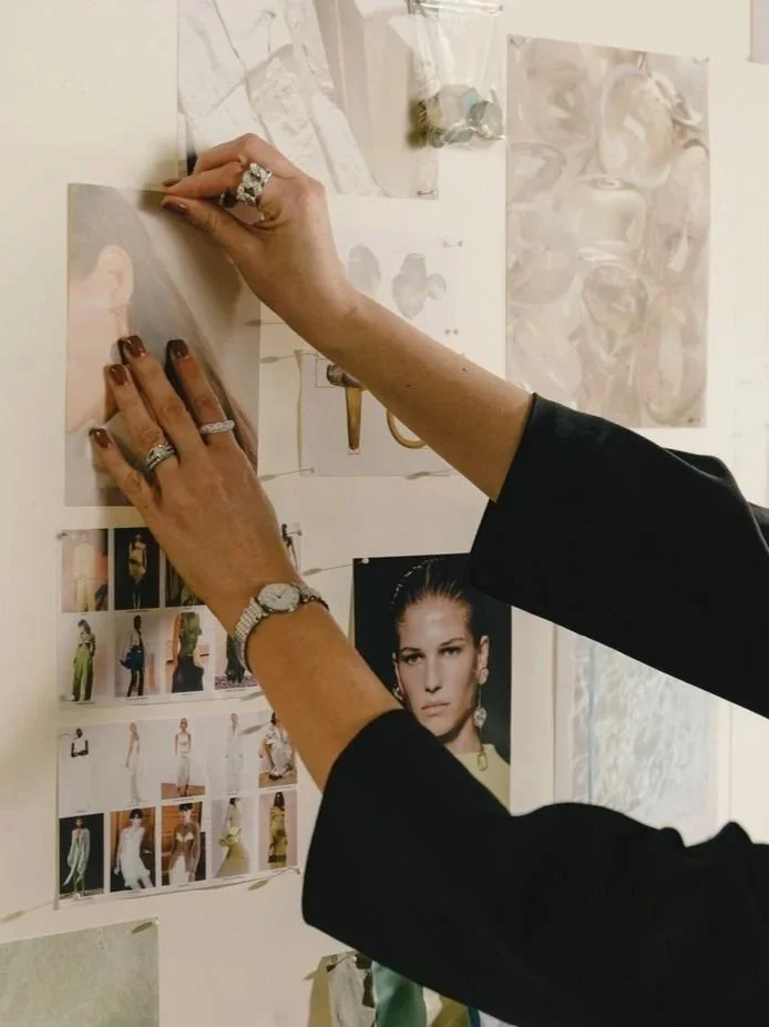Person pinning or attaching a photograph to a wall collage. The person is wearing rings and a watch, with black sleeves visible.