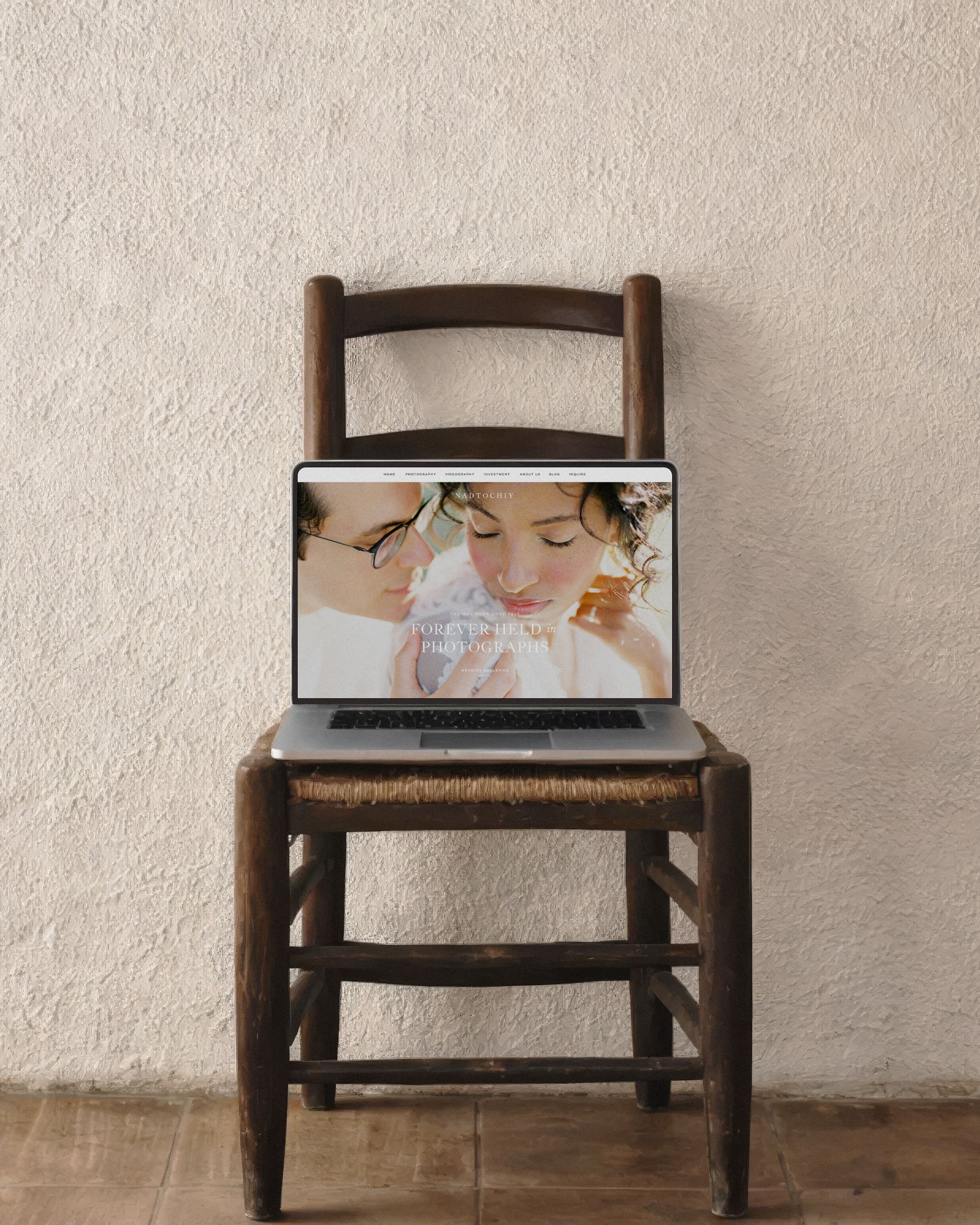 A laptop on a wooden chair against a textured beige wall, showing a photo of two women close together.