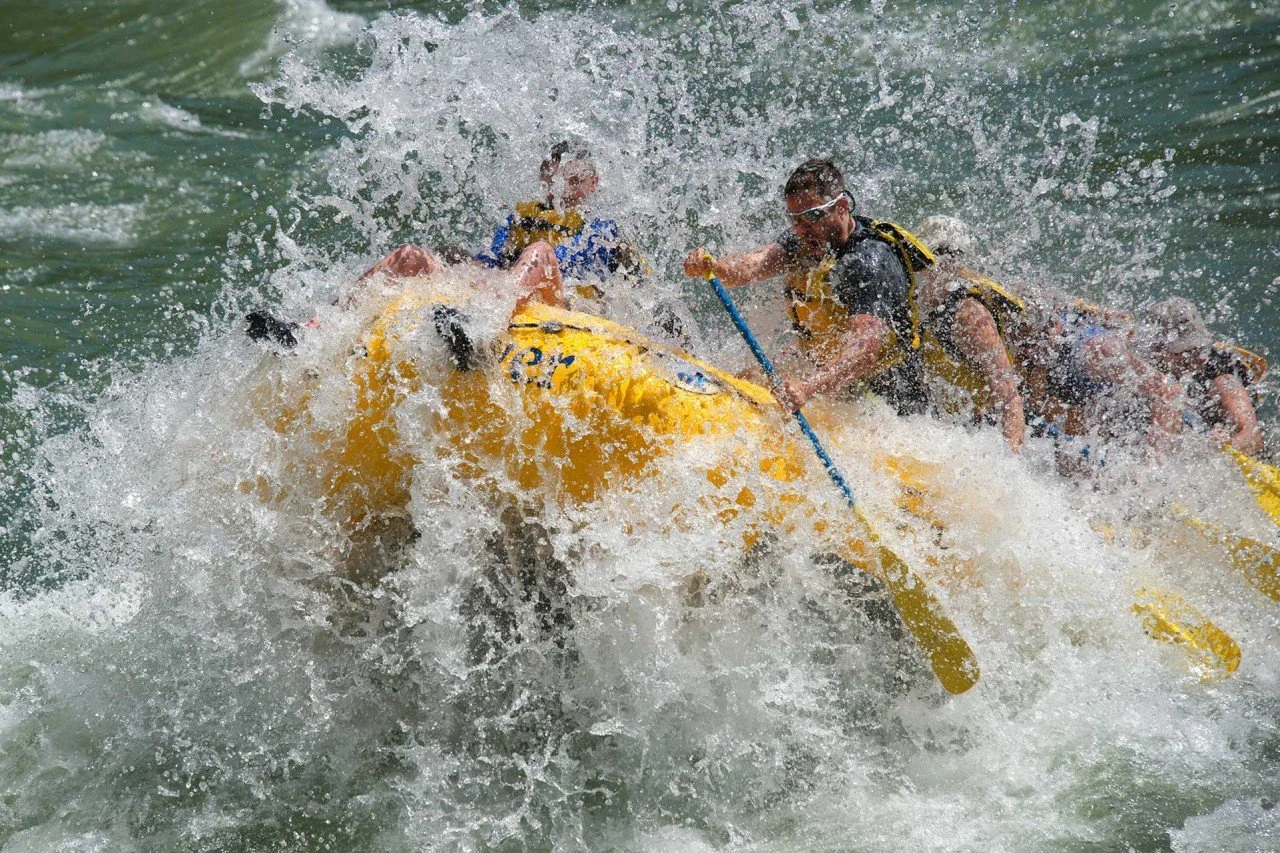 People white water rafting in a yellow inflatable raft, splashing water in an outdoor river setting.