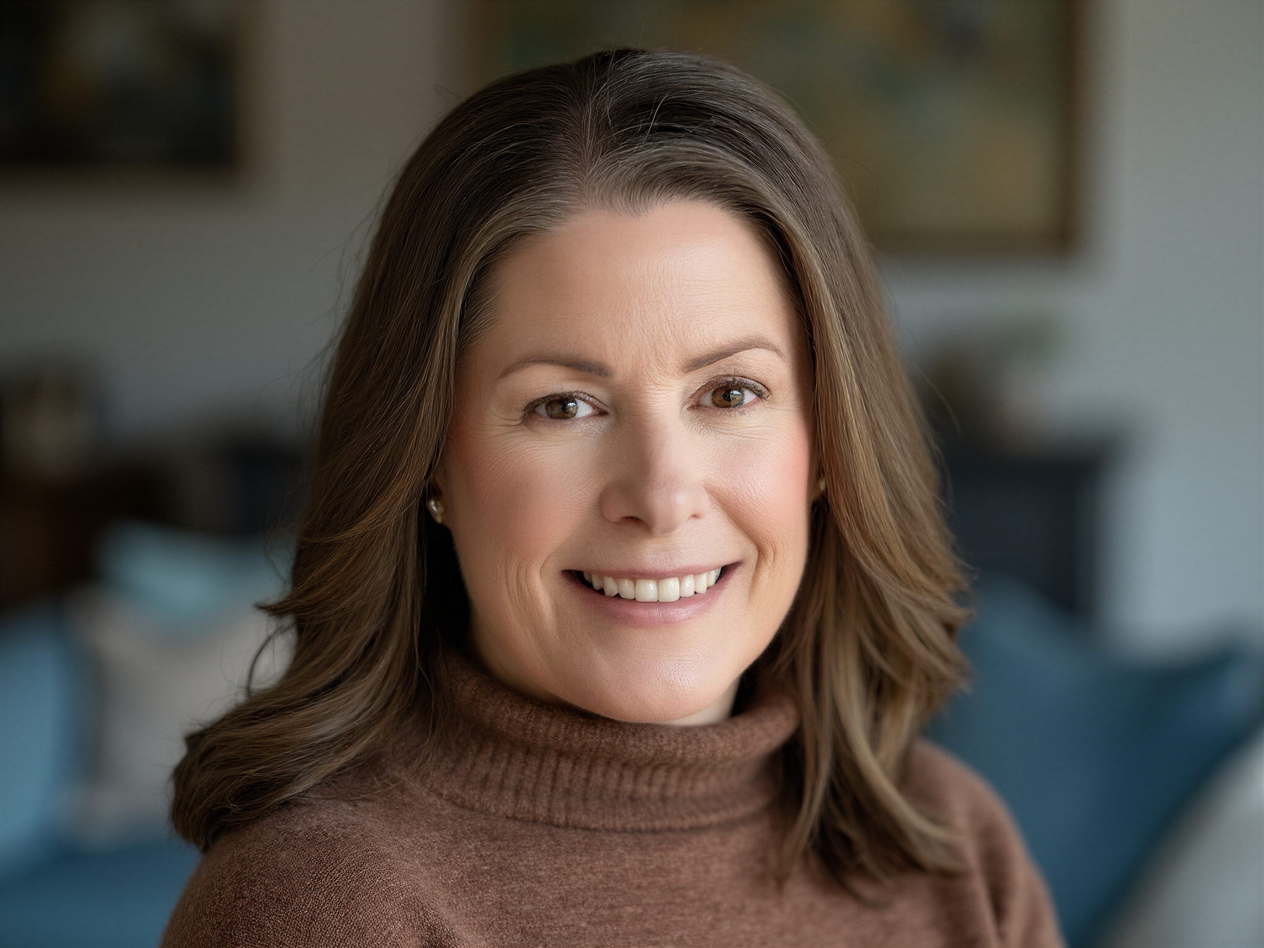 A woman with shoulder-length brown hair smiling indoors with a blurred background.