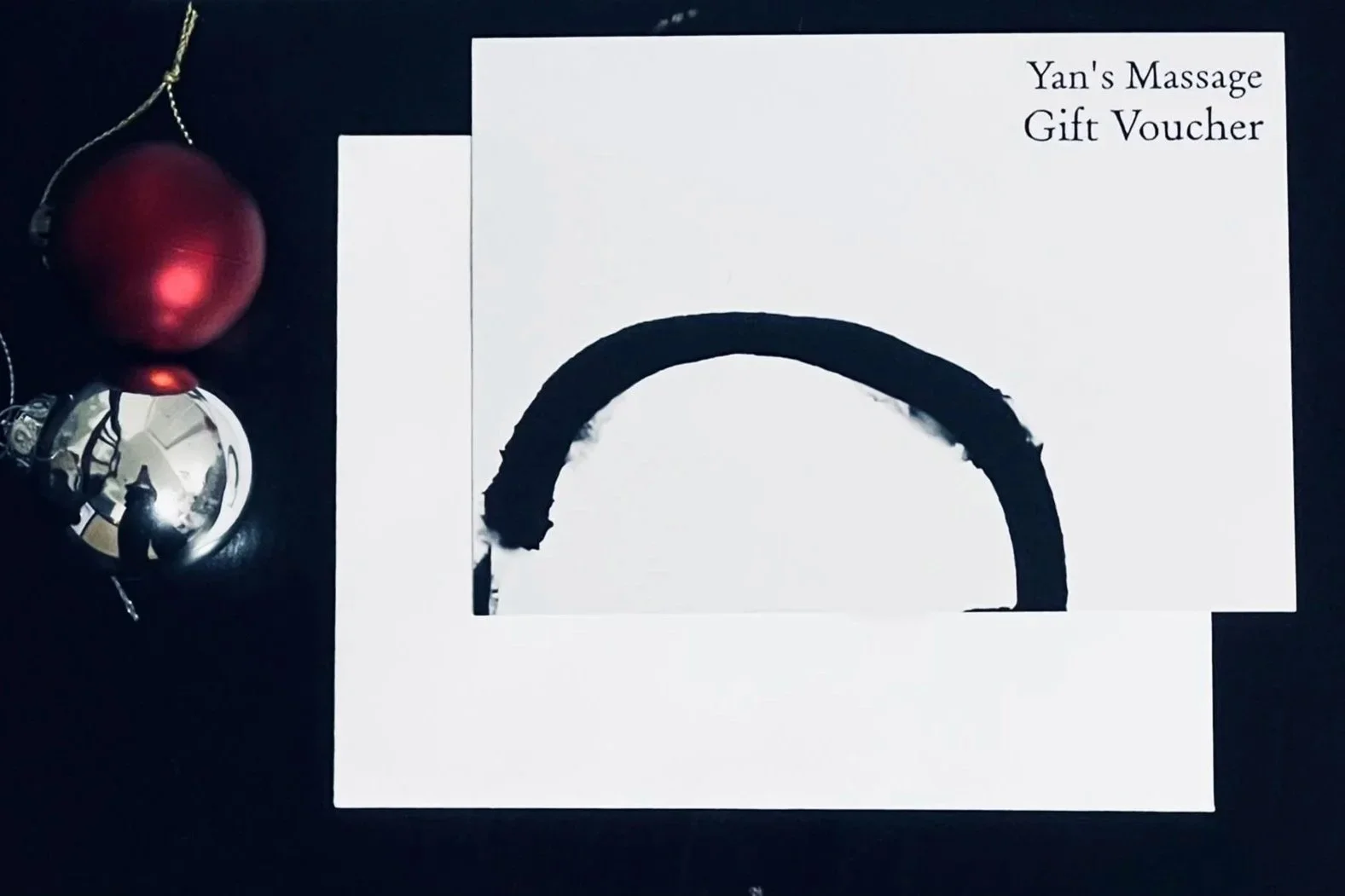 A gift voucher for Yan's Massage featuring a black painted semi-circle on white paper, with a Christmas ornament on the left side.