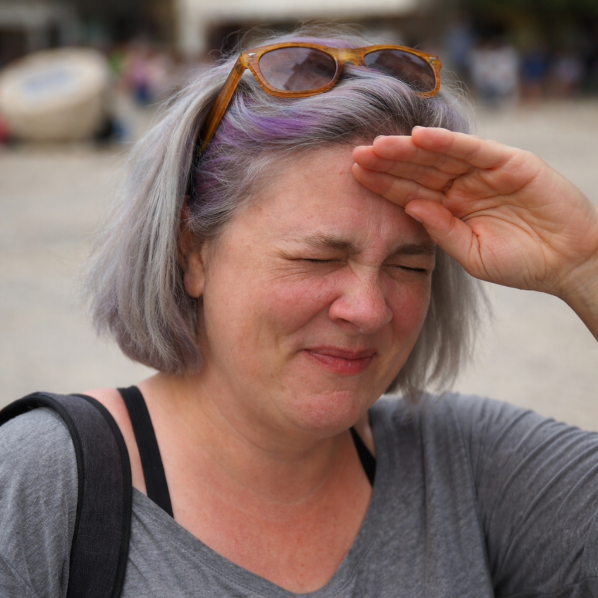 Sensory rest - A woman with short, gray hair, wearing sunglasses on her head, shielding her eyes from the sun and squinting.