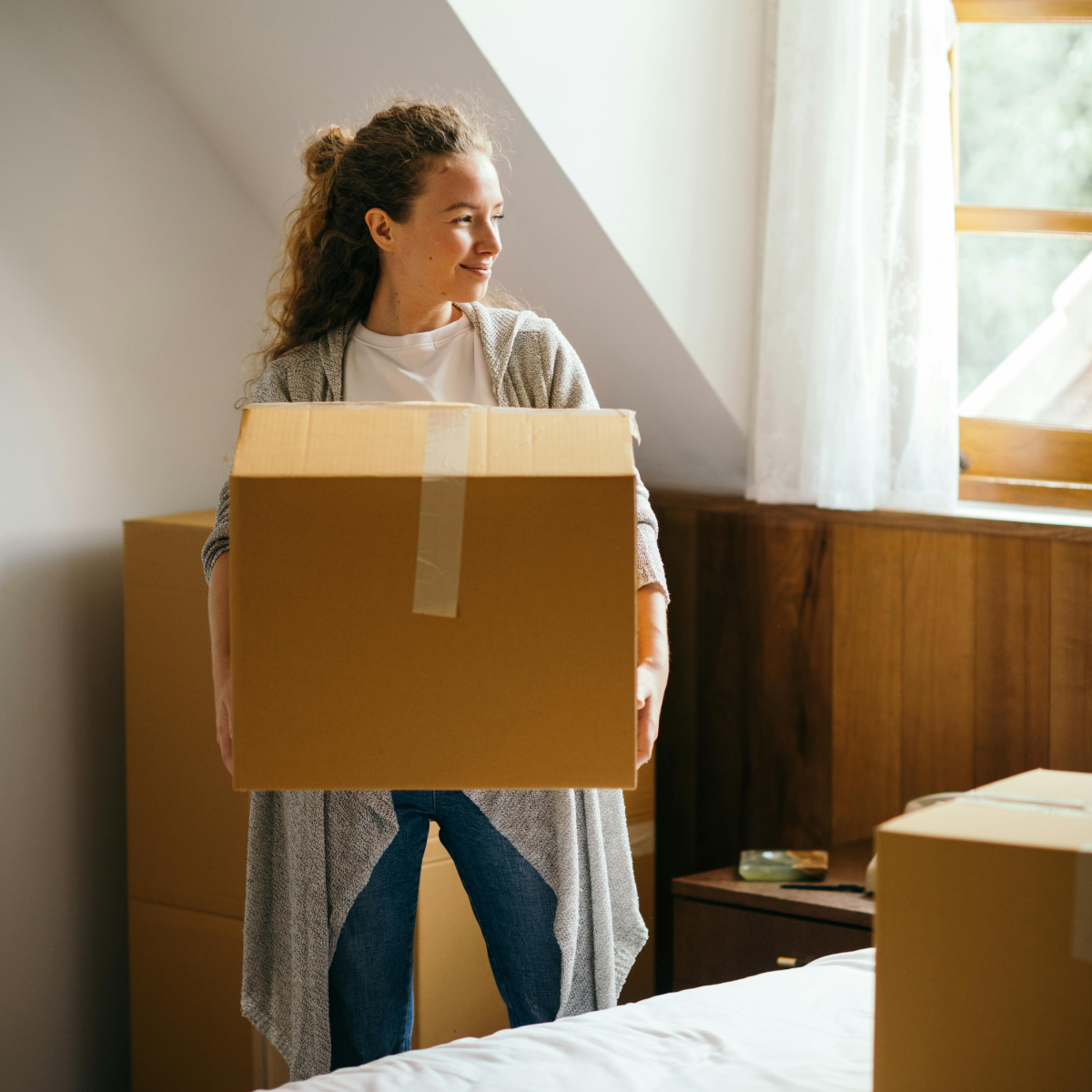 Photo of a smiling woman with moving boxes. Photo from Unsplash - Elyas Pasban