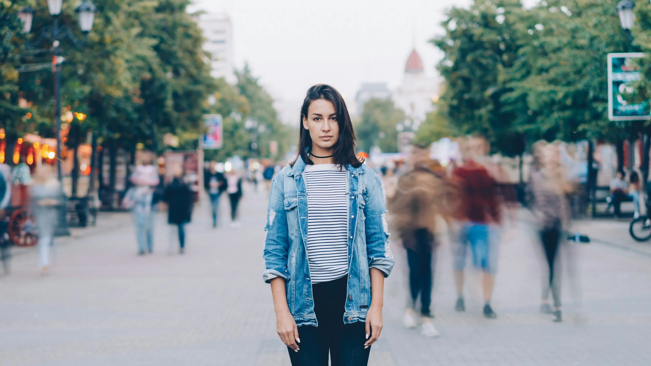 Photo of a young woman standing isolated in a crowd. Photo from Unsplash - Vitaly Gariev