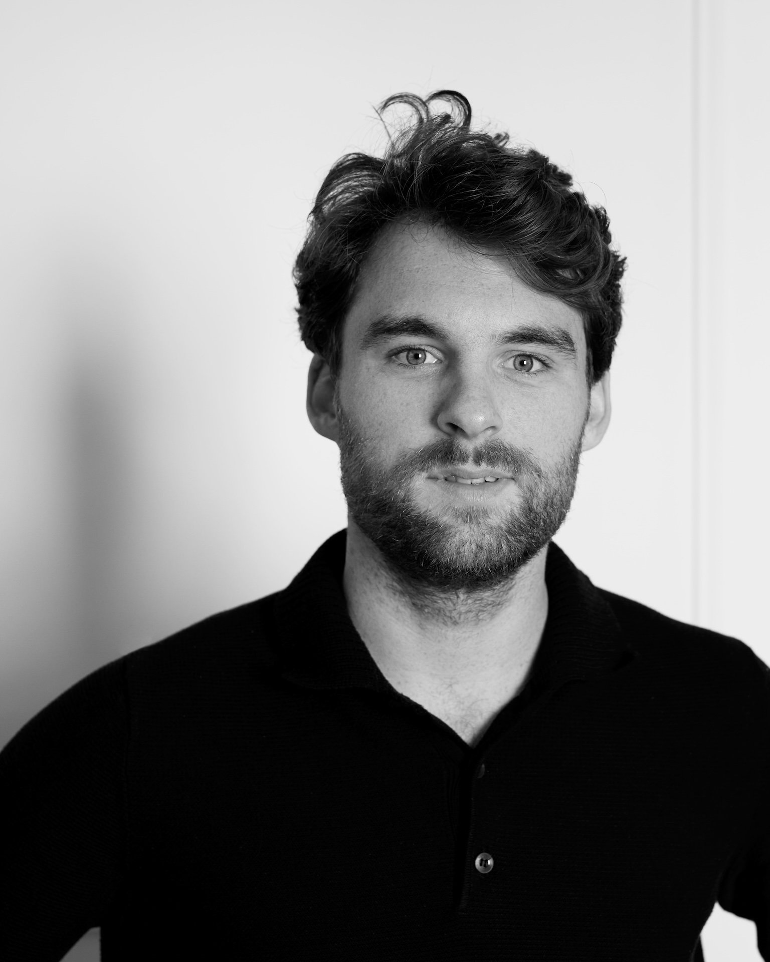 Portrait en noir et blanc d'un homme avec des cheveux bouclés et une barbe, portant un pull noir.