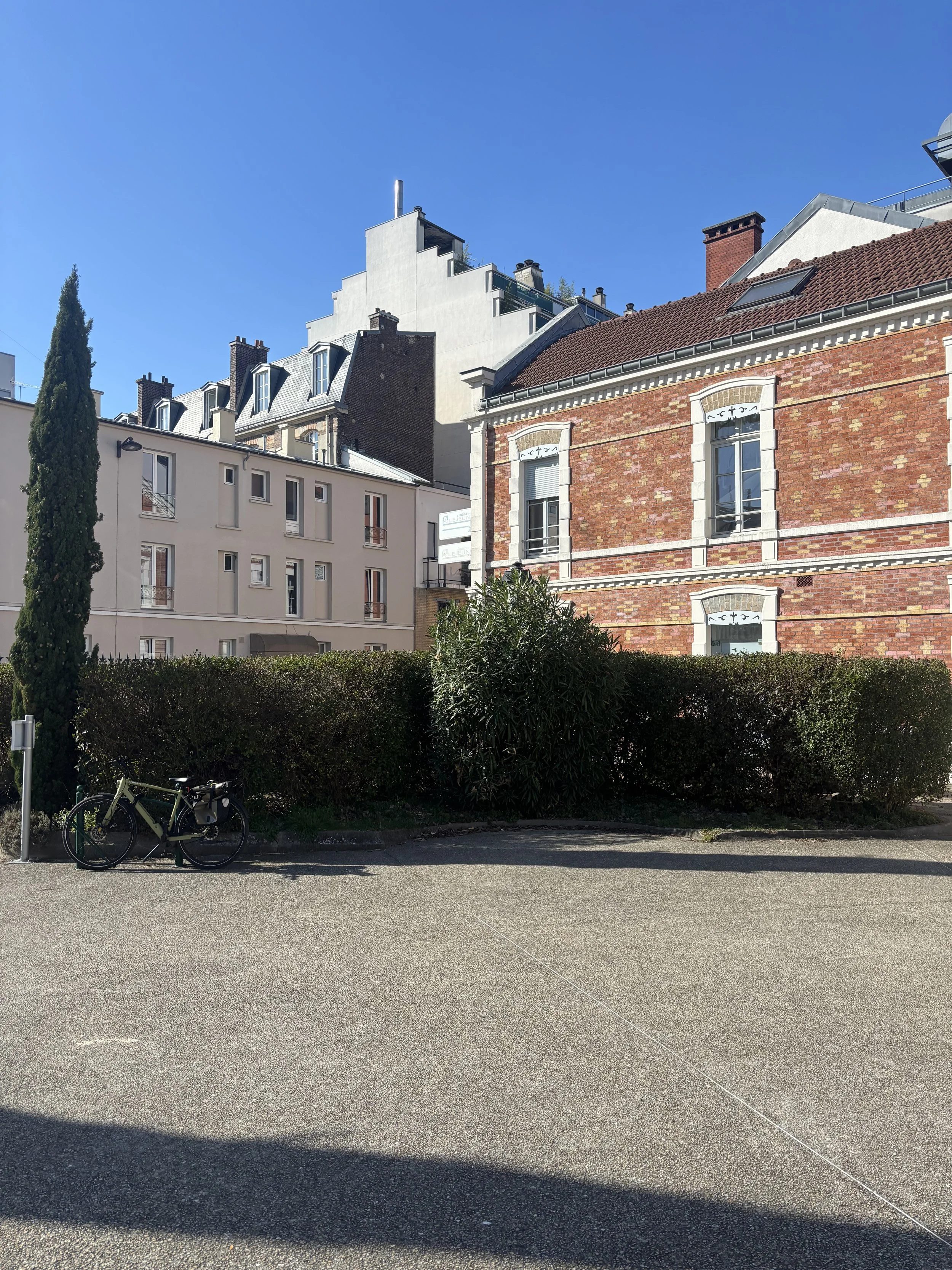 Vue d'un tramway station dans une ville, avec un vélo noir garé au premier plan et des bâtiments résidentiels en arrière-plan sous un ciel bleu clair.