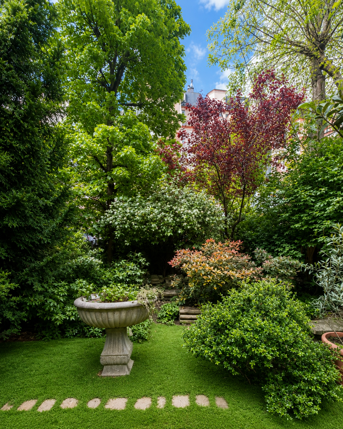 Un jardin fleuri avec des arbres, des arbustes, une fontaine en pierre, un gazon vert et un ciel bleu en arrière-plan.