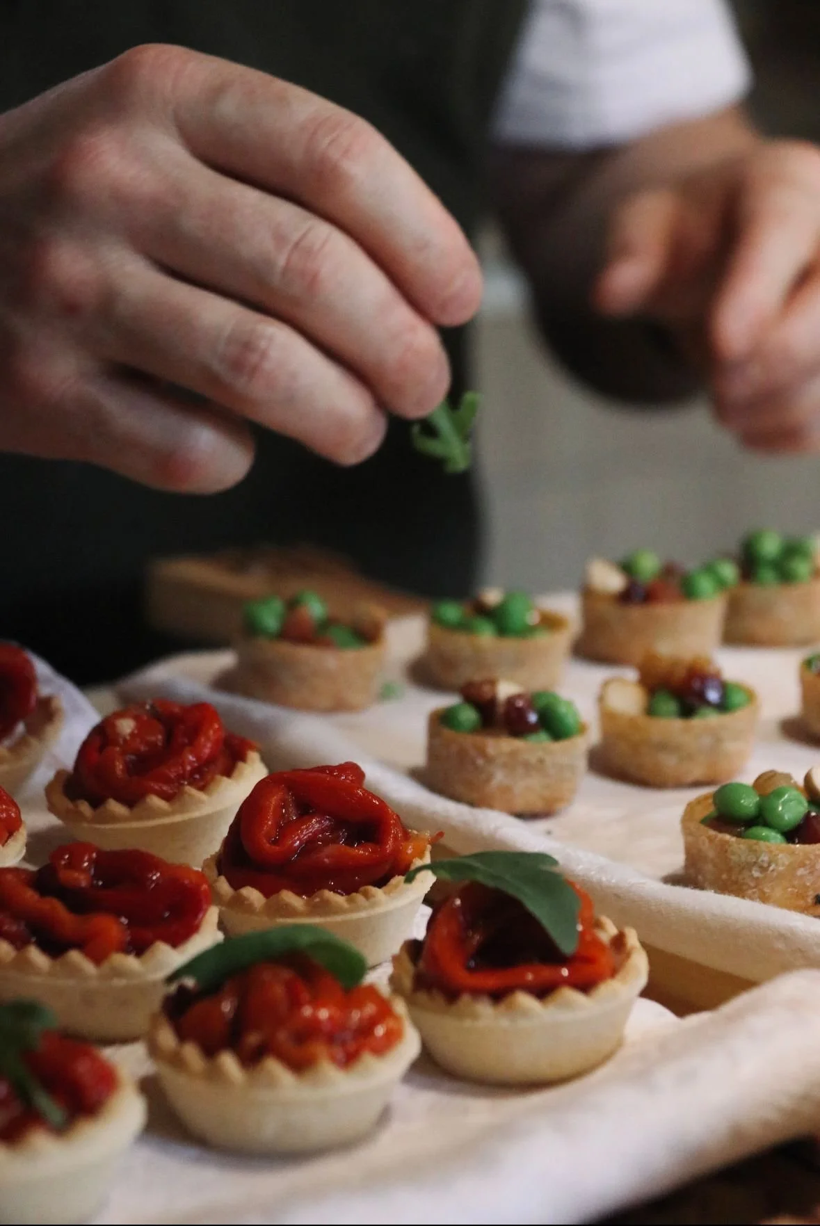 Hands packaging mini savory tartlets with red peppers and green peas.