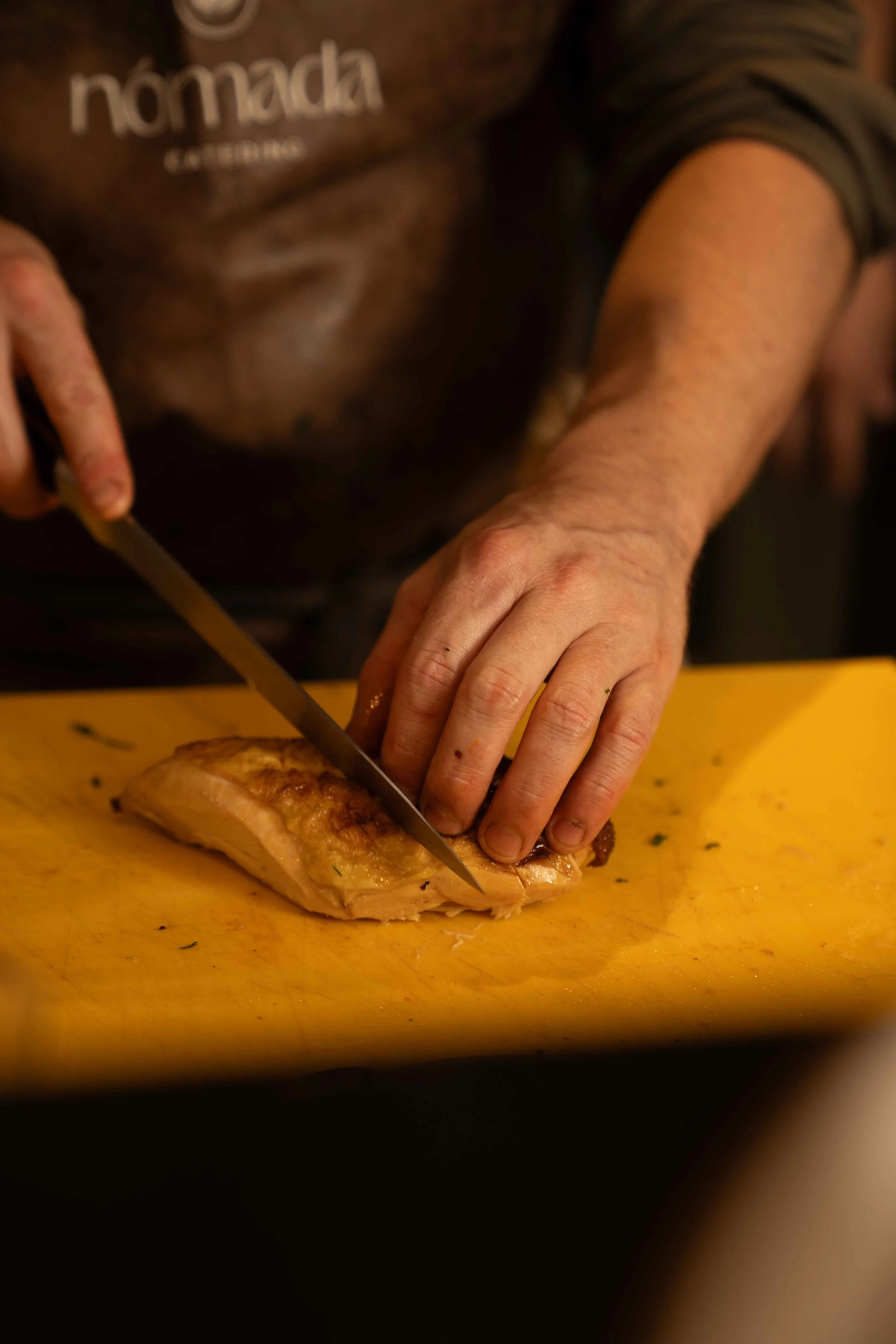 Person cutting cooked chicken on a wooden cutting board.