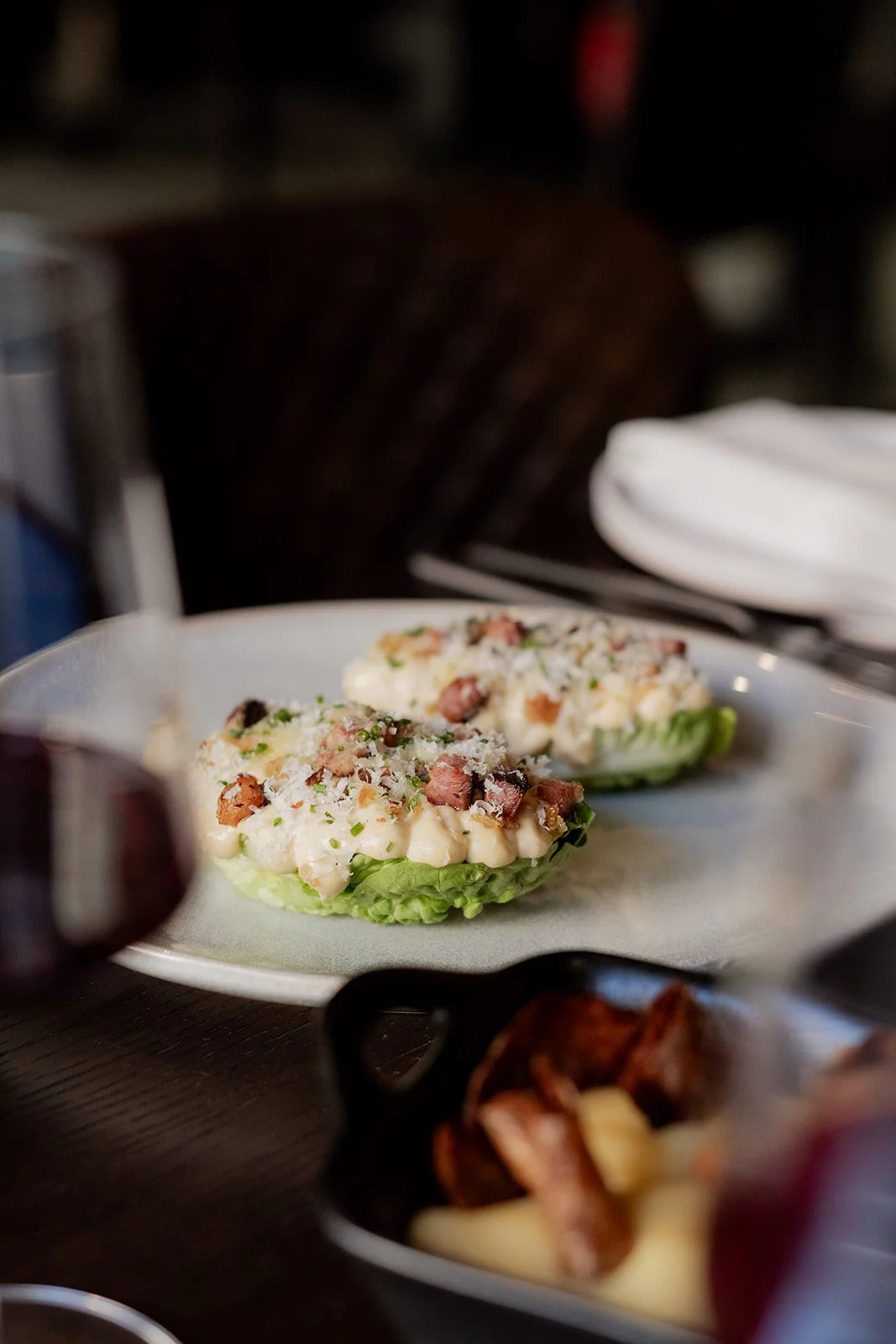 Two lettuce cups filled with creamy salad topped with bacon bits and shredded cheese on a white plate.