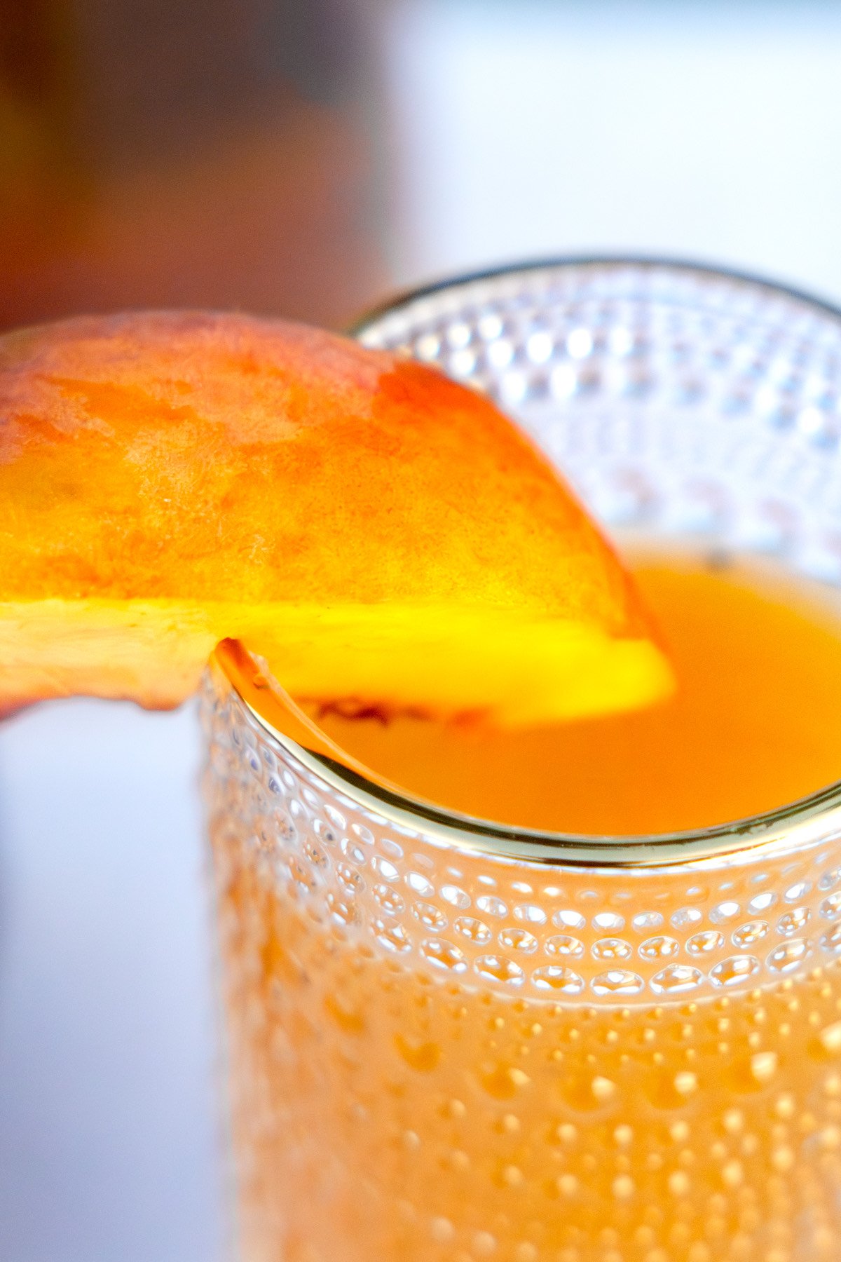 Close-up of a glass filled with orange-colored drink, garnished with a slice of orange on the rim.