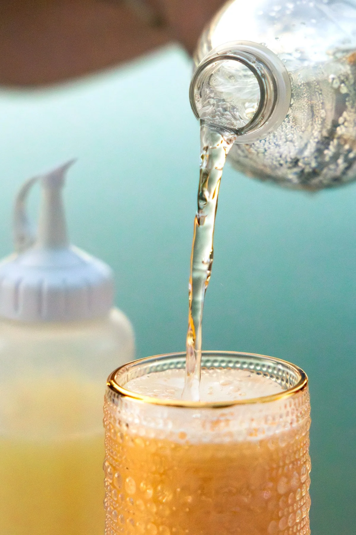 A bottle of sparkling water being poured into a glass with a gold rim, with condensation on the glass.