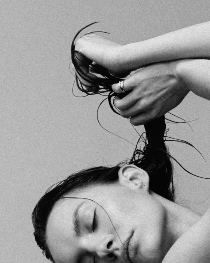A woman with closed eyes is holding and lifting her wet hair.